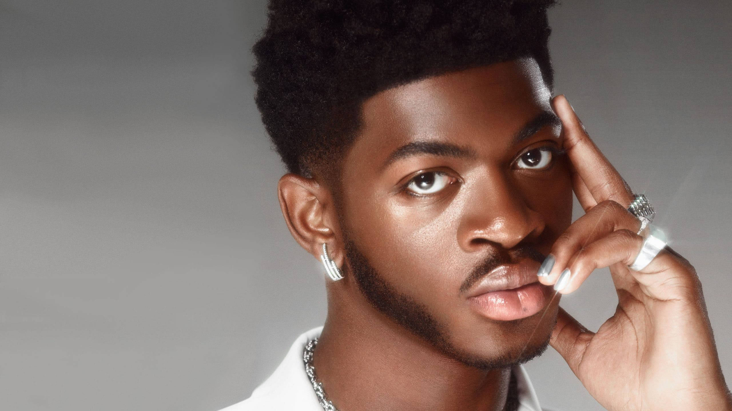 Lil Nas X 個人肖像拍攝 壁紙 — 一位自信的年輕男子，留著非洲式髮型，佩戴銀飾，在灰色攝影棚背景前擺姿勢。