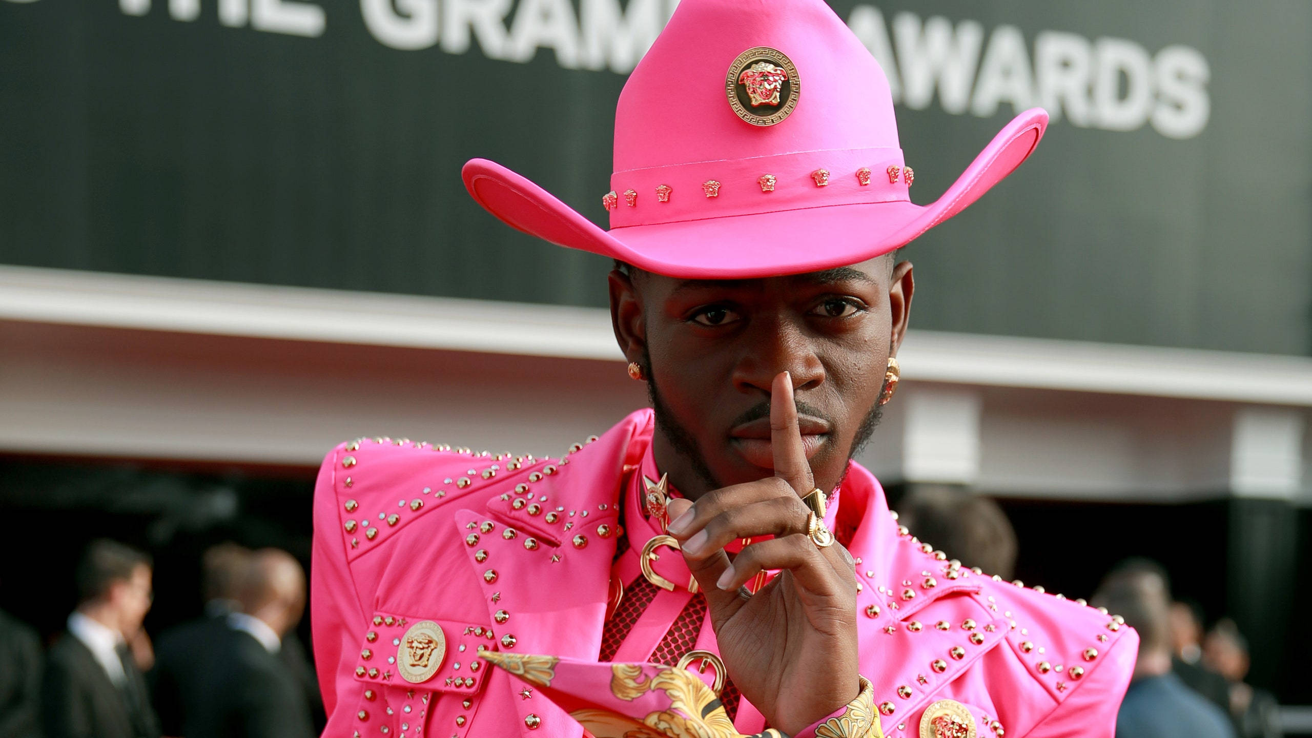 Lil Nas X 熱粉紅夢幻造型 壁紙 — 一名戴著大膽粉紅色牛仔帽和鉚釘外套的男子在格林美獎上做出噤聲手勢。