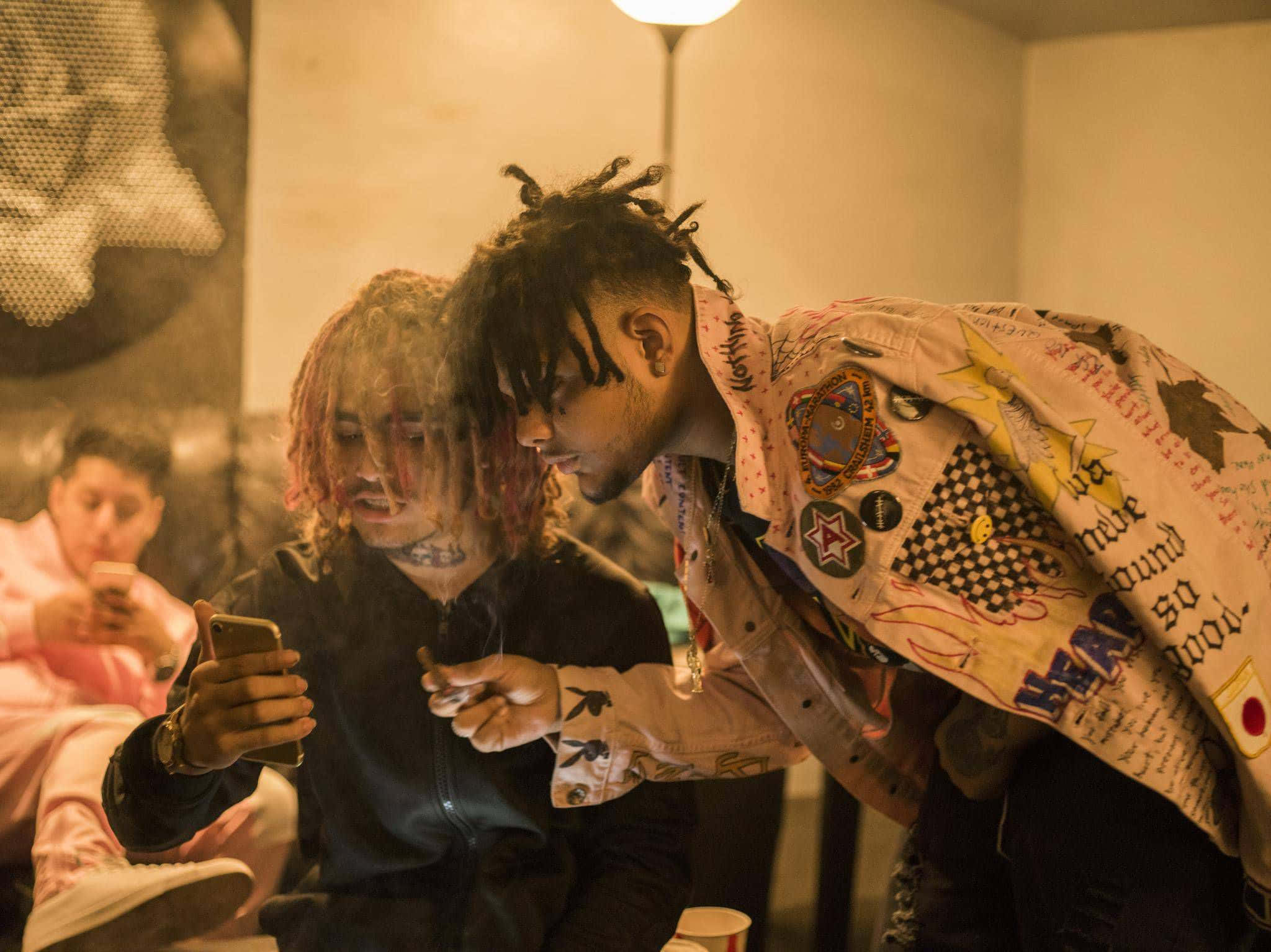 Lil Pump 舞台演出 壁紙 — 兩名頭髮色彩繽紛的年輕男子在溫暖照明的室內空間中傾身觀看手機屏幕。