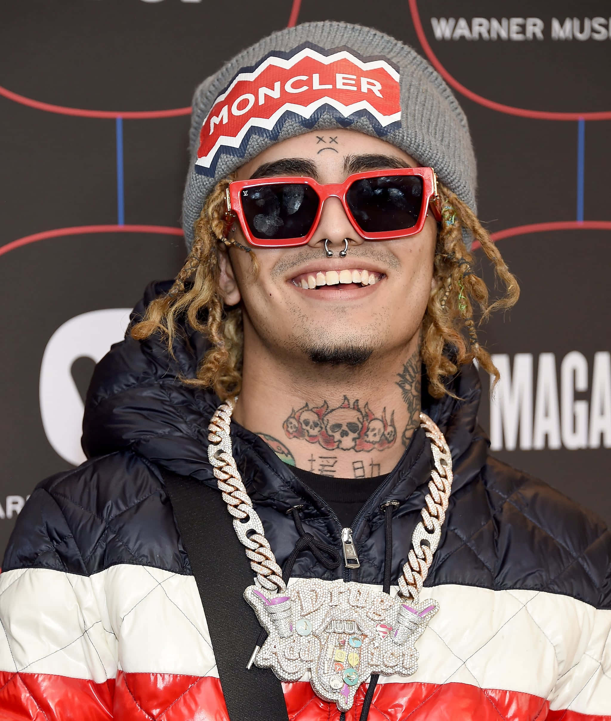 說唱歌手、詞曲創作人兼唱片製作人 Lil Pump 壁紙 — 一位面帶微笑、留著辮子的男士，戴著紅色太陽眼鏡、Moncler 冷帽，以及一件搶眼的紅白黑羽絨外套，配上一條大鏈條項鍊。