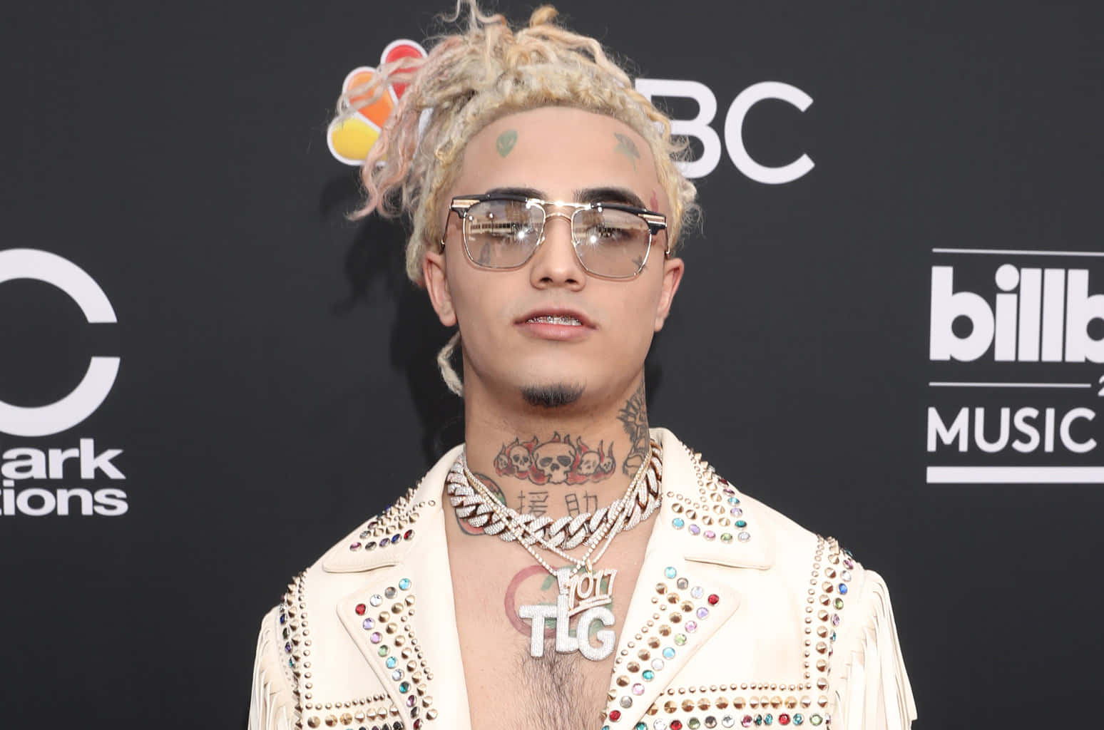Lil Pump 登台演出 壁紙 — 一名金髮辮子、戴太陽眼鏡的男子，在Billboard音樂獎紅地毯活動中穿著飾有鉚釘的白色外套。