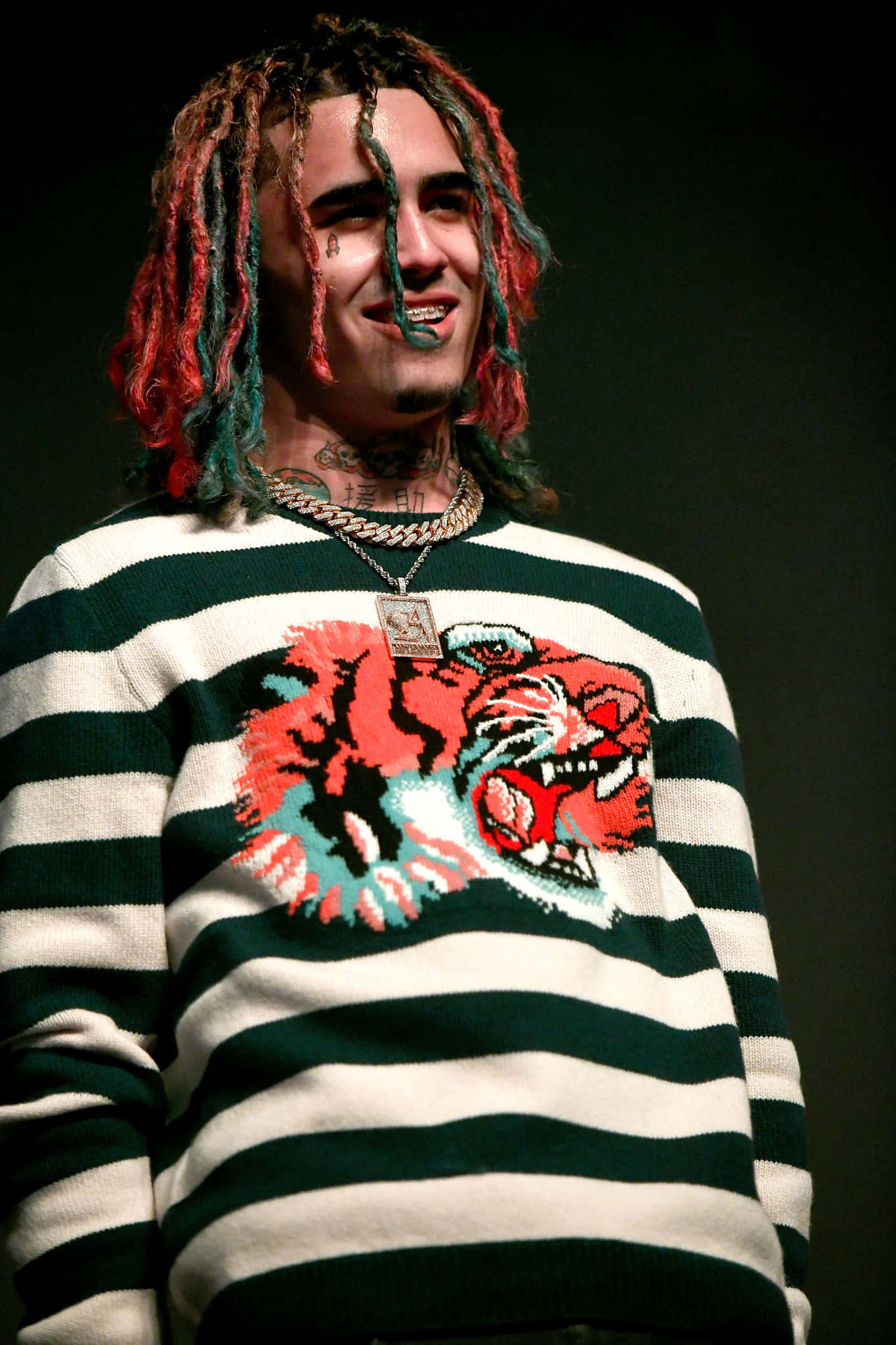 Lil Pump 舞台演出 壁紙 — 一名擁有彩色辮子的男士微笑著，身穿帶有醒目紅色老虎圖案的綠色和白色條紋毛衣。