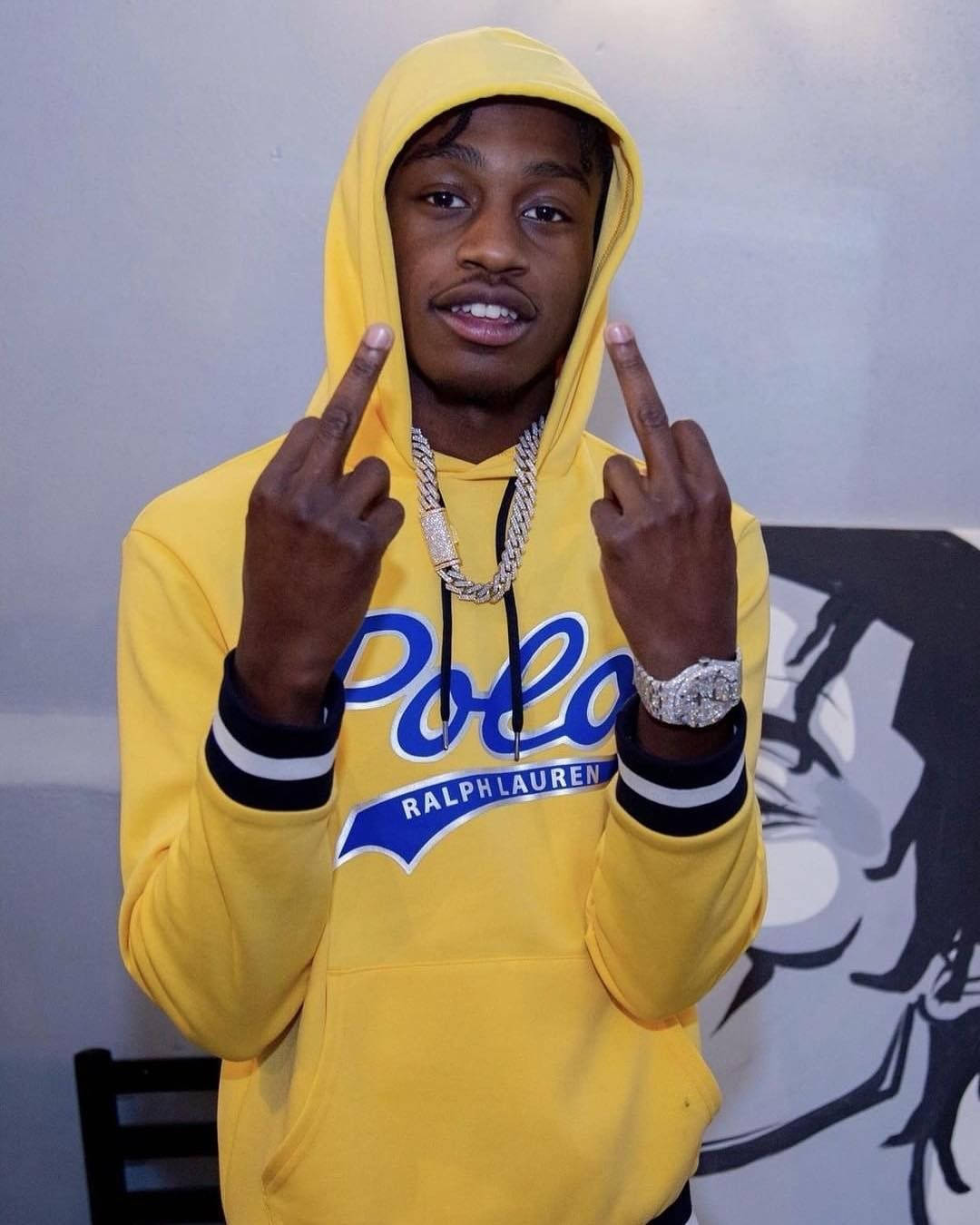Lil Tjay 黃色連帽衫 壁紙 — 一名年輕男子穿著亮黃色Ralph Lauren連帽衫，豎起雙手中指，戴著粗鏈條和鑲鑽手錶。