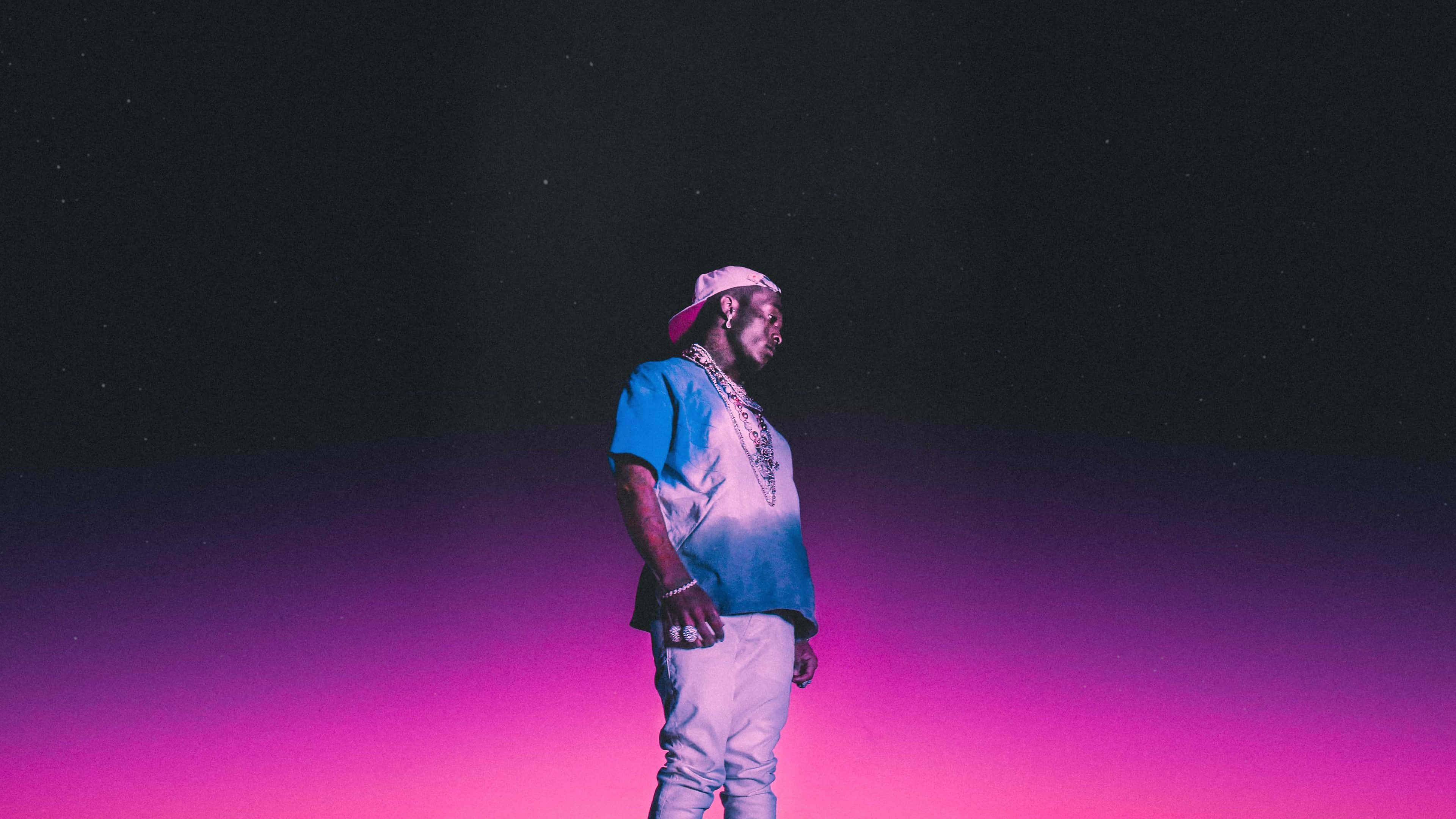 Lil Uzi Vert 4K 桌面主題 壁紙 — 一個穿著藍色襯衫和白色帽子的人，在充滿星星的鮮豔粉紅和紫色漸變天空下形成剪影。