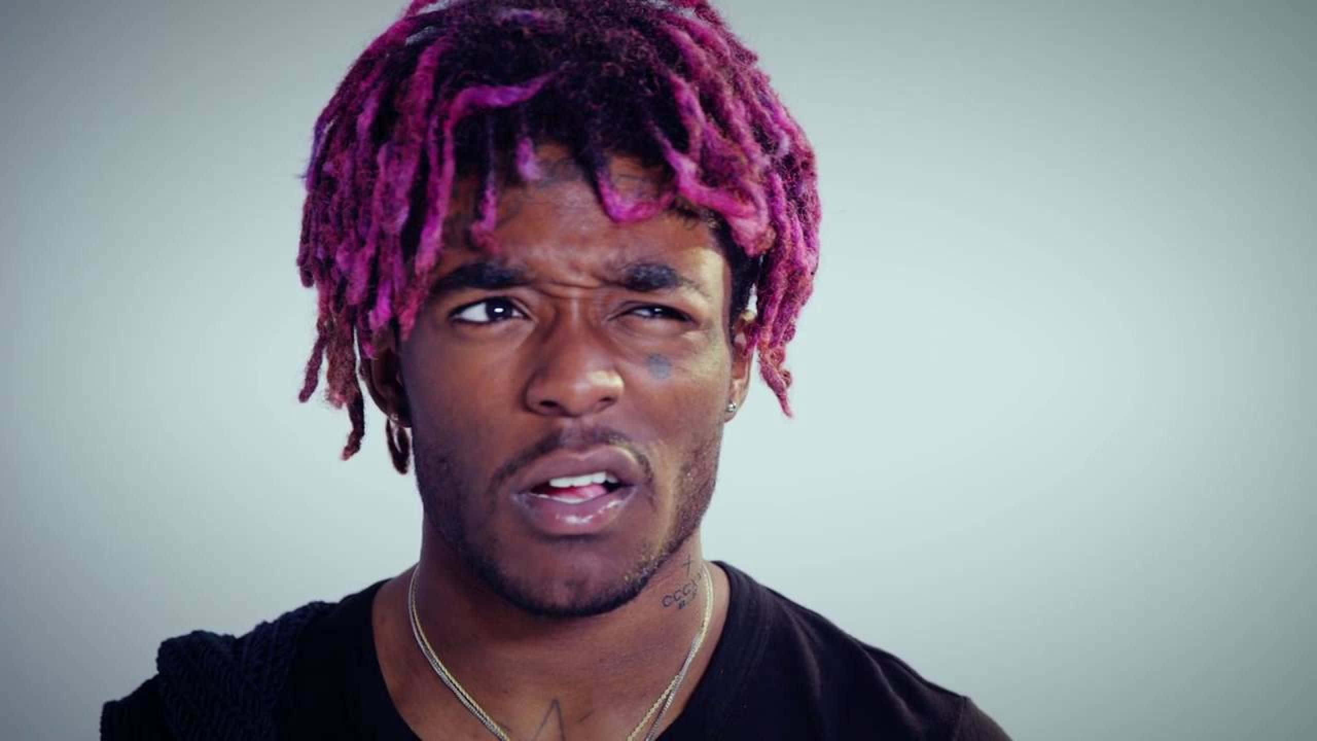 Lil Uzi Vert 混淆表情頭像 壁紙 — 一名擁有充滿活力的粉紅色辮子的男子，在樸素的灰色背景下強烈凝視。