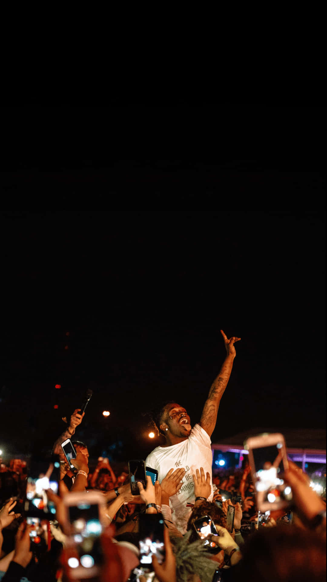 Lil Uzi Vert 發行《Eternal Atake》 壁紙 — 一位有紋身的表演者在夜晚高舉一隻手臂，勝利的姿態高於人群，粉絲們用發光的手機錄影。