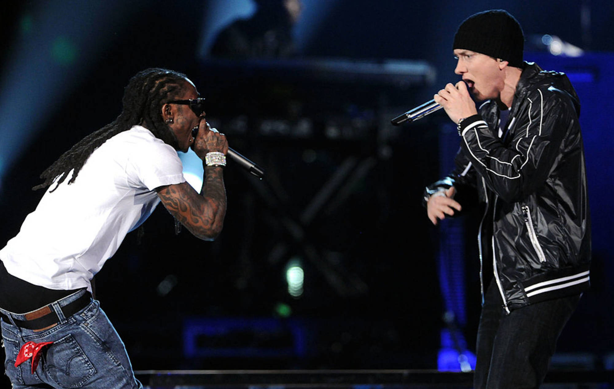 Lil Wayne 與 Eminem 饒舌演出 壁紙 — 兩位說唱歌手在燈光昏暗的舞台上，手持藍色聚光燈和麥克風，進行激烈的表演。
