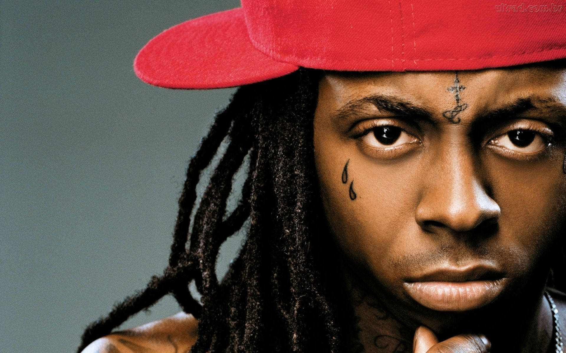 Lil Wayne舞台演出 壁紙 — 灰色背景前，一名留著辮子、戴紅色帽子、臉上有紋身的男子的特寫肖像。