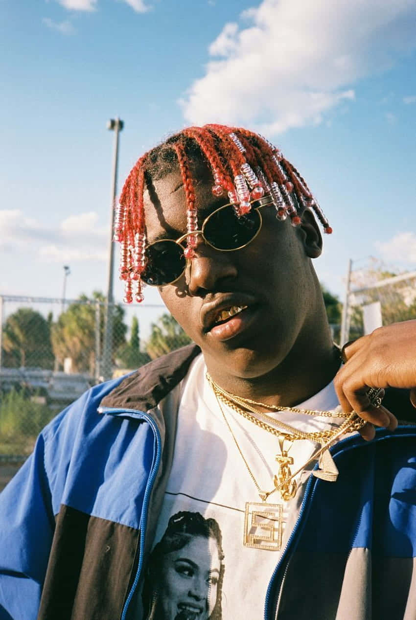 Lil Yachty：饒舌歌手與創作人 壁紙 — 一位年輕男子戴著紅色珠辮和金鏈，在明亮的藍天下自信地戶外擺姿勢。