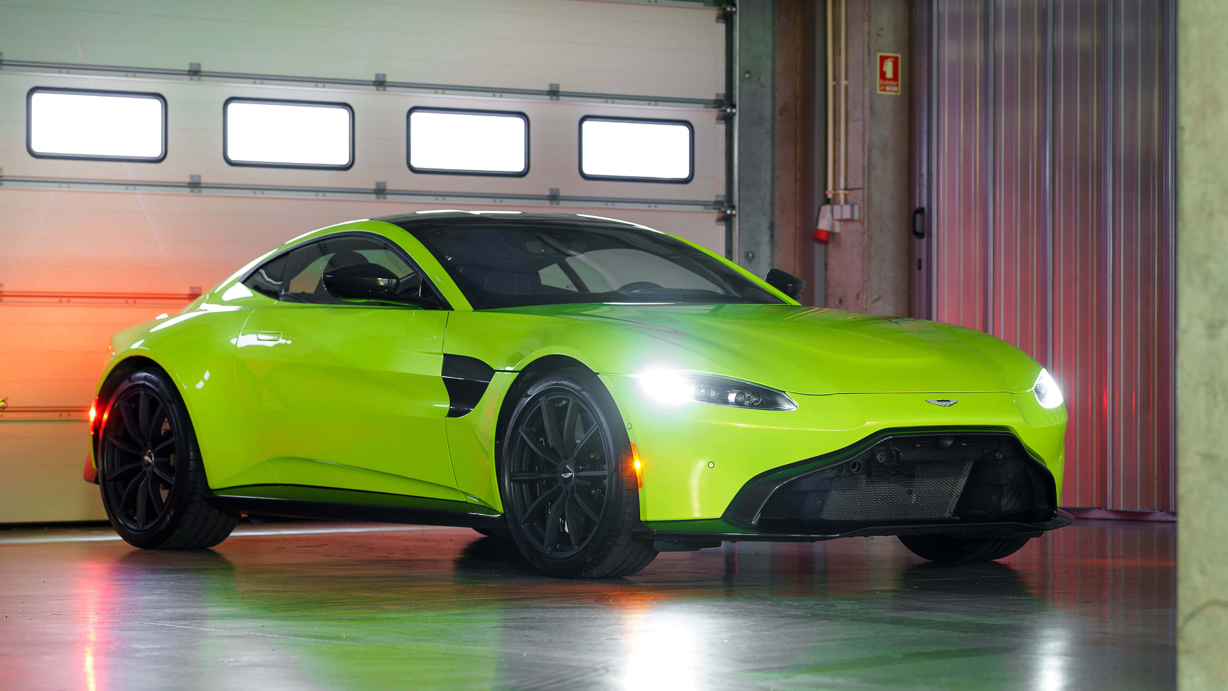 Aston Martin Vantage 桌布 壁紙 — 一輛充滿活力的青檸綠色 Aston Martin Vantage 在車庫燈光下閃耀，帶有黑色飾邊和發光的車頭燈。