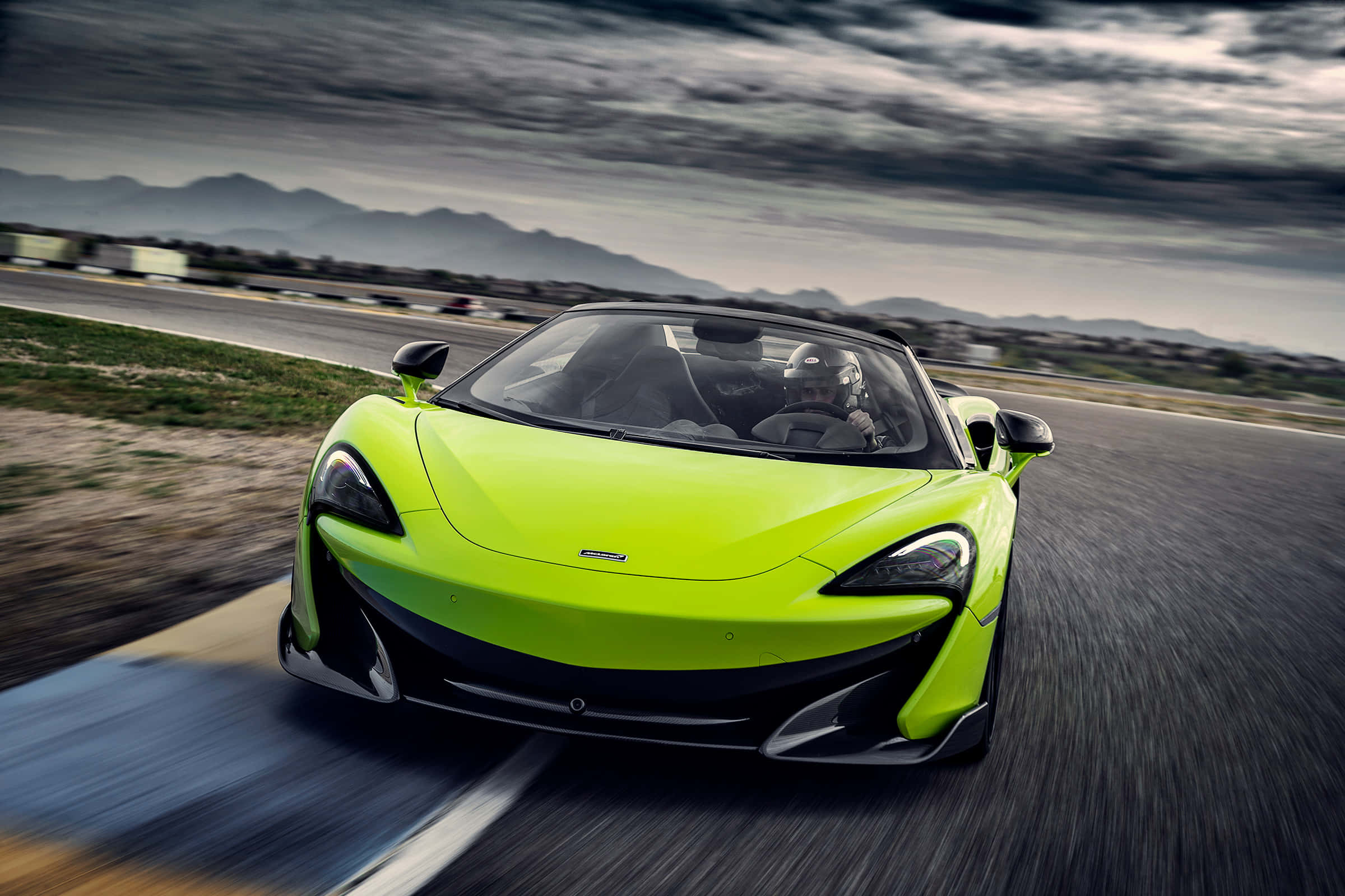 Mclaren 600lt Spider 桌布 壁紙 — 一輛充滿活力的青檸綠色McLaren 570S開篷跑車在戲劇性的多雲天空下，以模糊的動態在賽道上飛馳。
