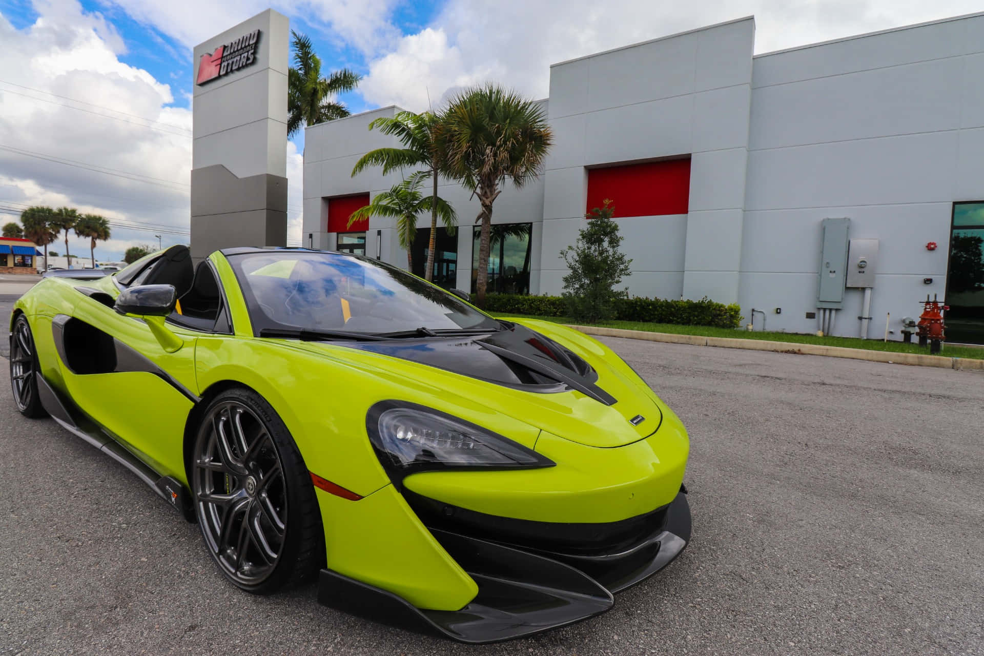 Mclaren 600lt Spider 桌布 壁紙 — 一輛充滿活力的青檸綠色McLaren跑車停泊在現代化經銷商外，有棕櫚樹和部分多雲的天空。