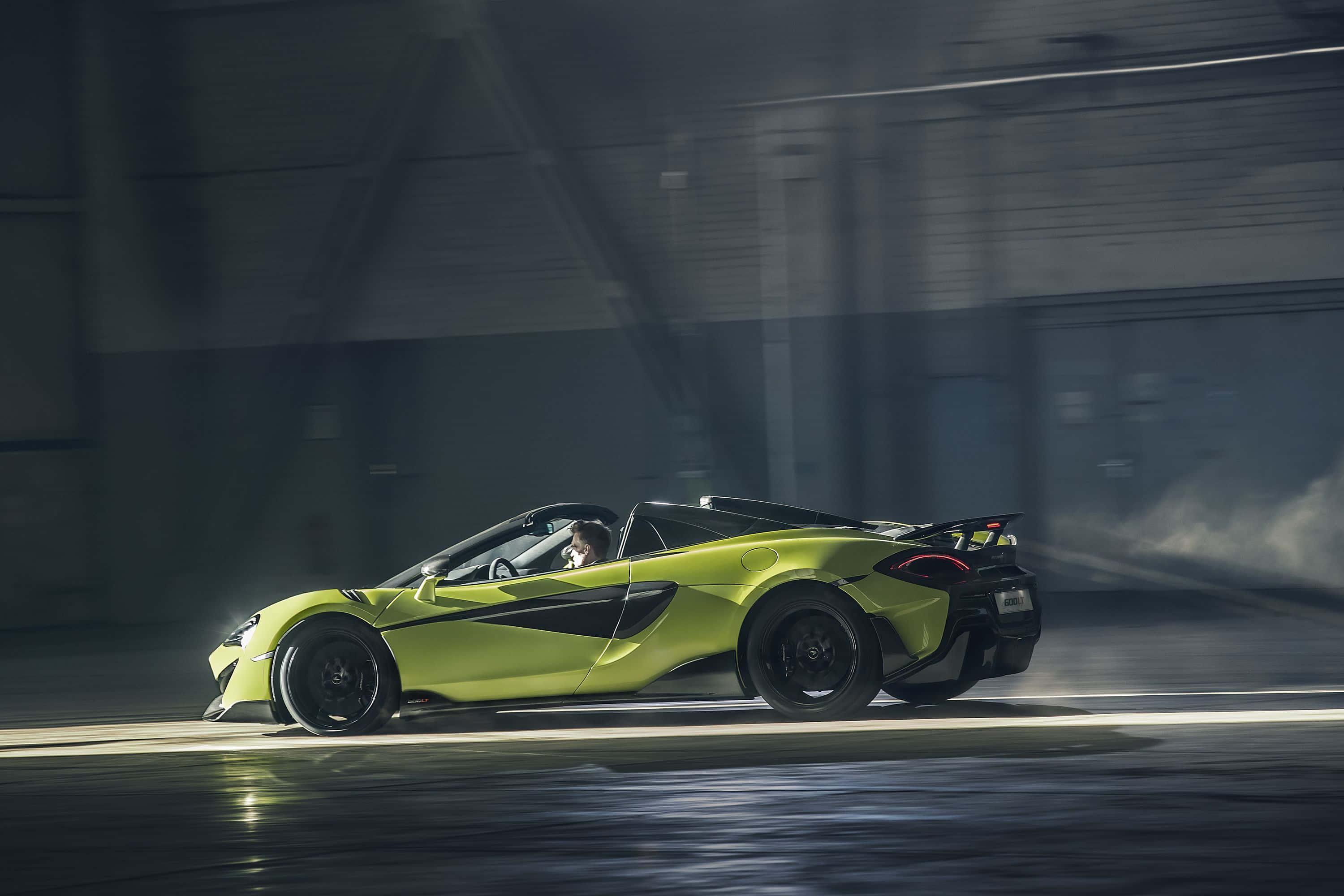 Mclaren 600lt 桌布 壁紙 — 一輛青檸綠色的McLaren跑車在昏暗的工業車庫中疾馳，帶有動態模糊和戲劇性燈光。