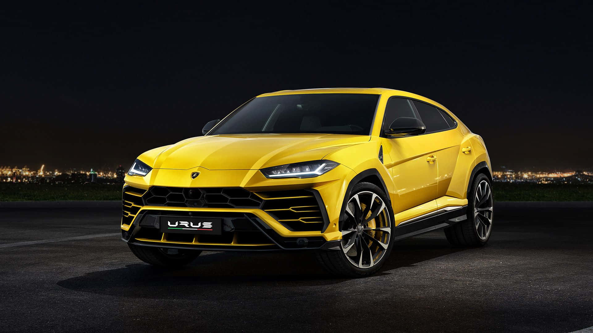 Lamborghini Urus 桌布 壁紙 — 一輛鮮黃色的林寶堅尼 Urus SUV 在夜燈下閃耀，背景是發光的城市天際線。