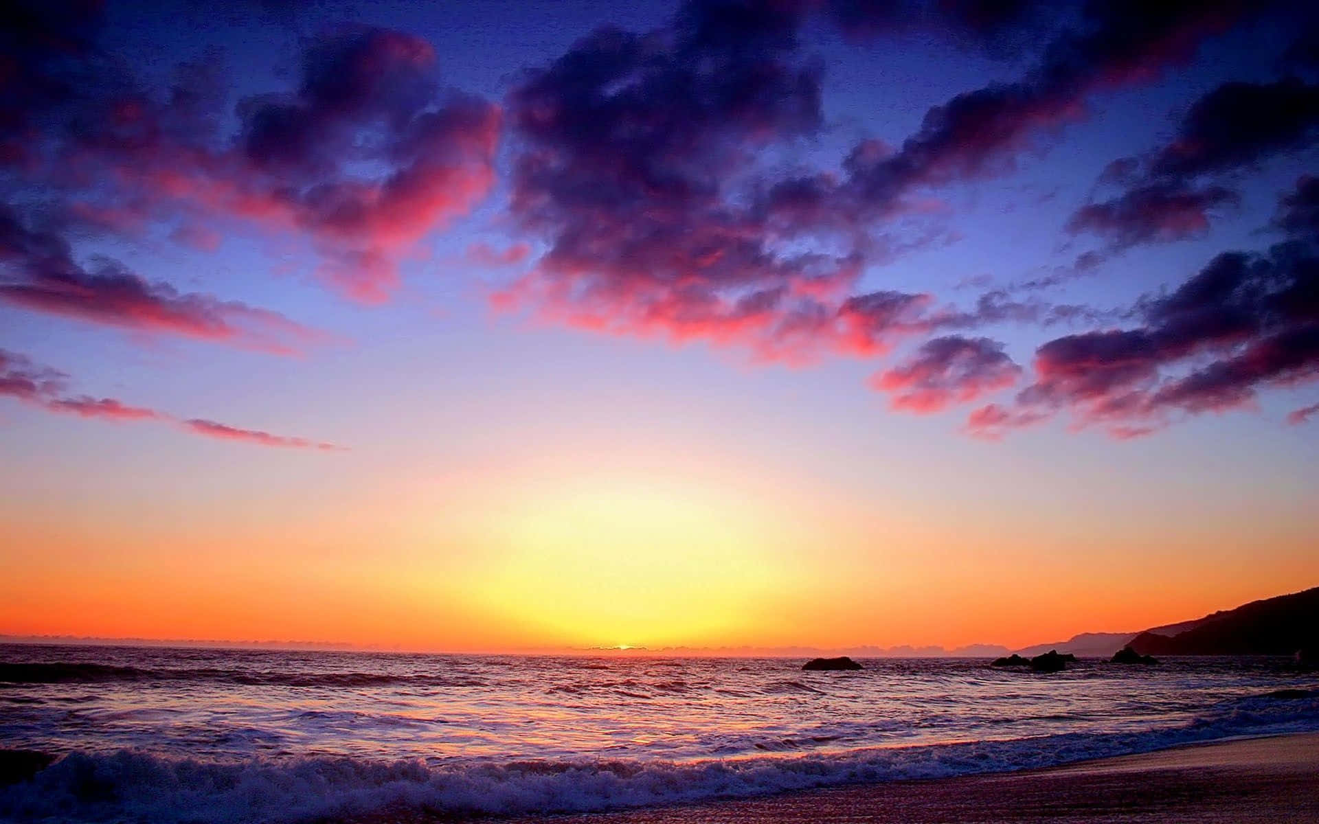 Colorful Sunset 桌布 壁紙 — 令人屏息的日落將天空染成火熱的橙色和深紫色，海浪拍打著沙灘。