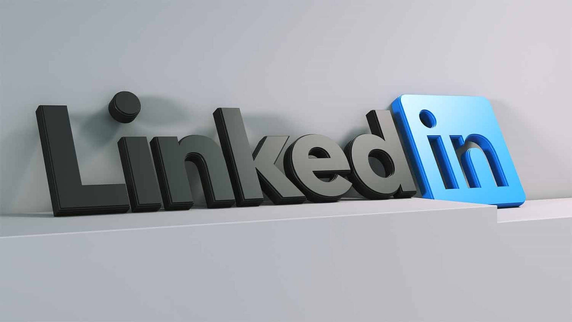 LinkedIn 3D 標誌 壁紙 — 3D 渲染的 LinkedIn 標誌，帶有金屬灰色字母和藍色方形圖標，放置在白色底座上，背景為淺灰色牆壁。