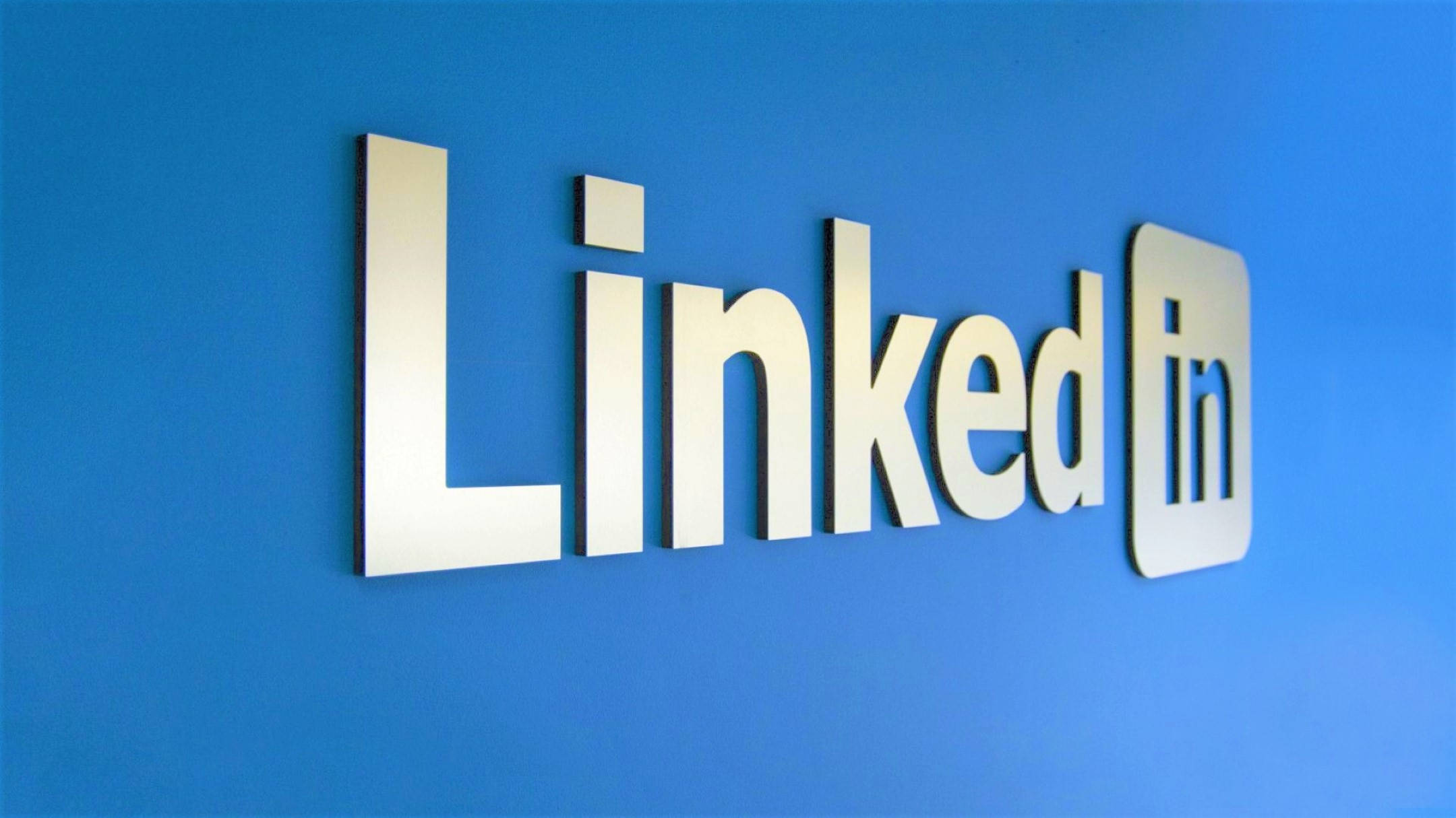 LinkedIn 墙面設計 壁紙 — 一個時尚的金屬LinkedIn標誌安裝在現代辦公室環境中充滿活力的藍色牆壁上。