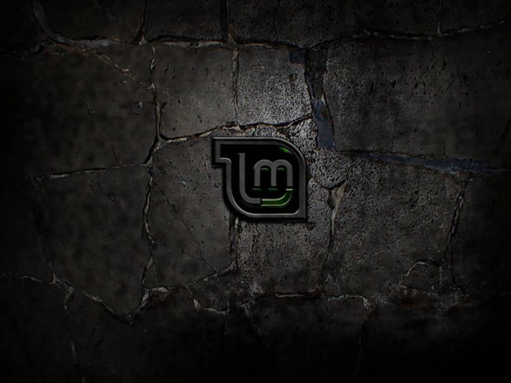Linux Mint 操作系統標誌於裂紋混凝土背景 壁紙 — 在戲劇性燈光下，嵌入裂縫暗石牆中的發光綠色風格標誌。