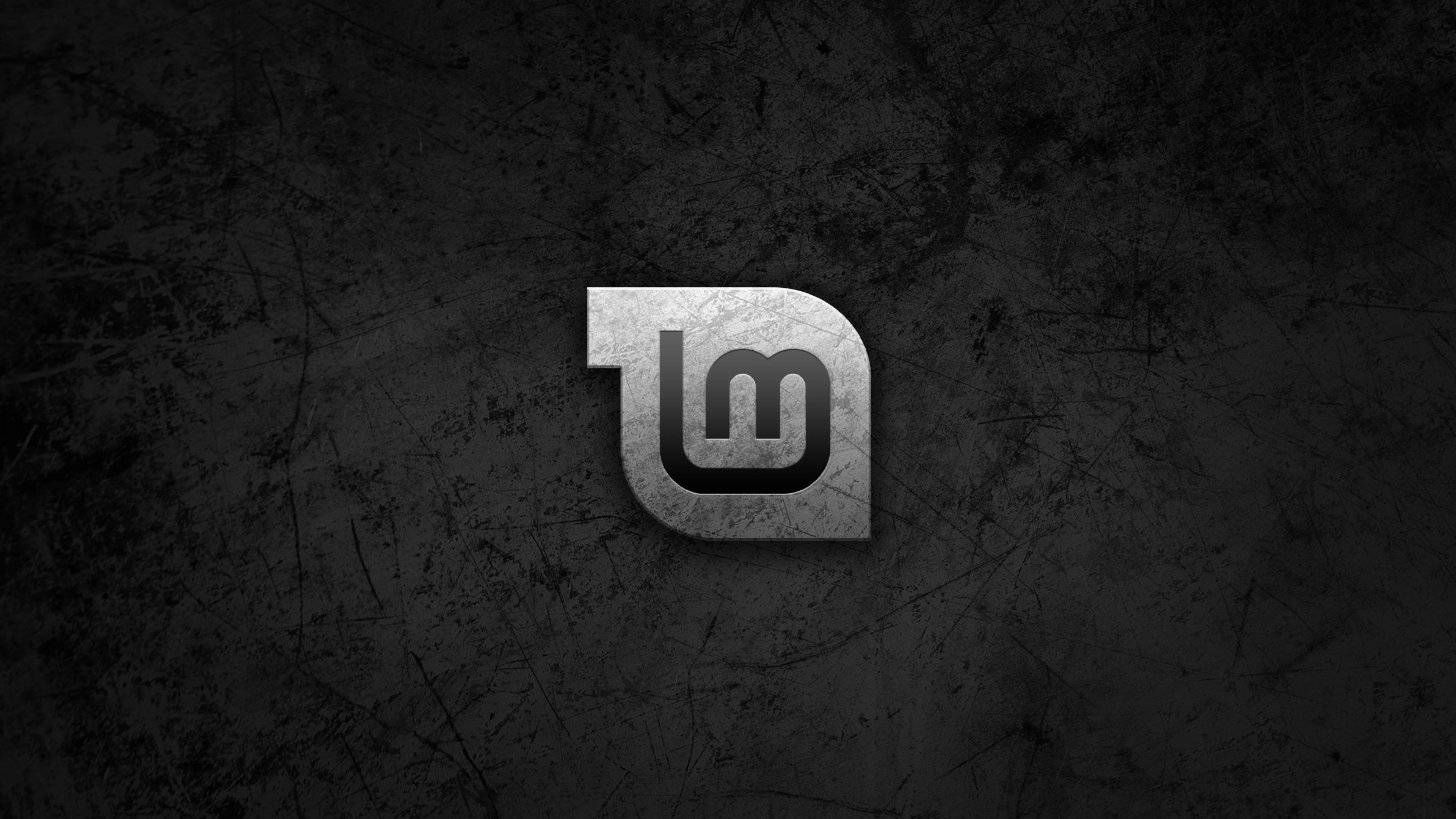Linux Mint 操作系統灰色刮痕標誌 壁紙 — 一個金屬標誌，中央有交織的字母「lm」，位於深色刮花牆壁背景上。