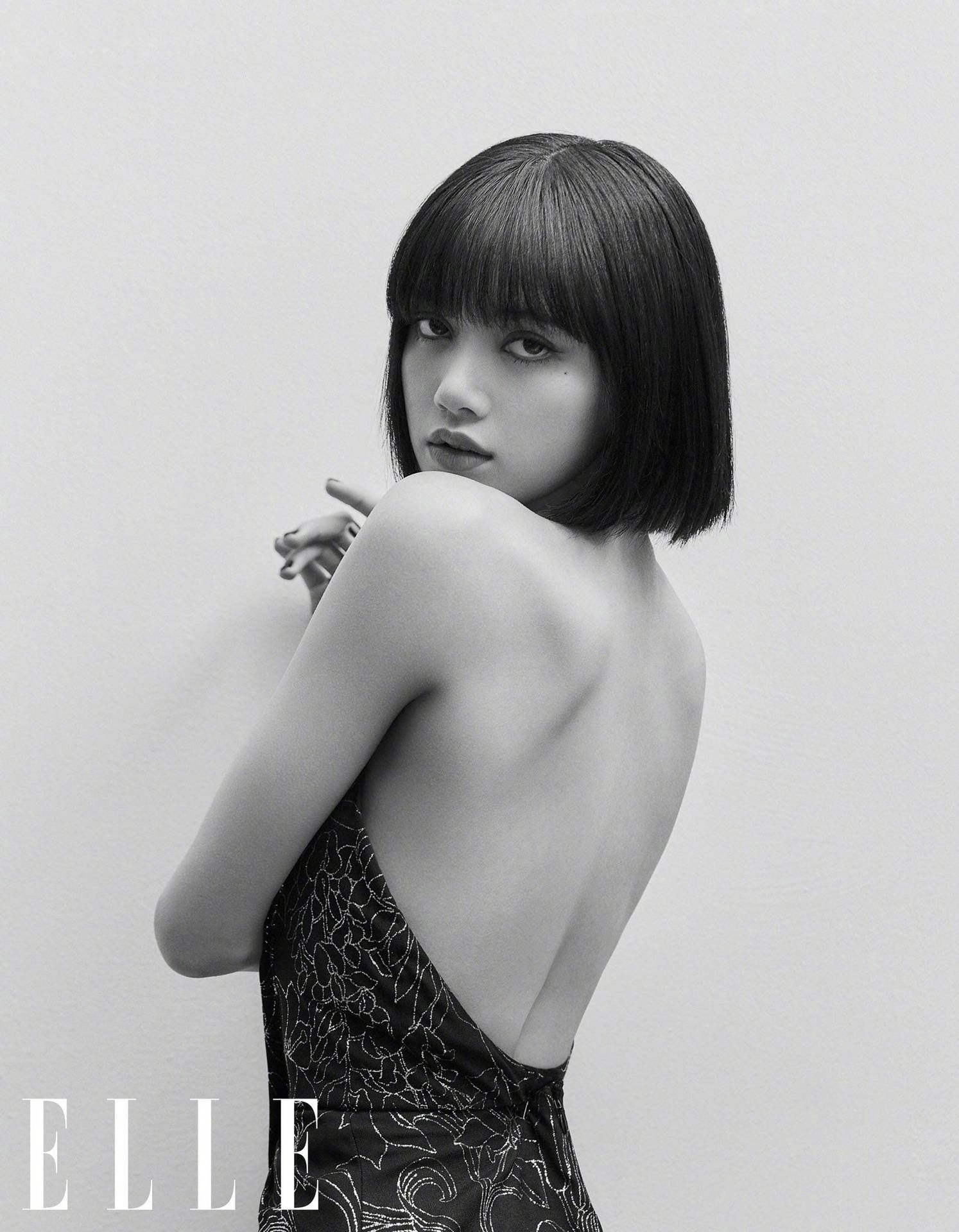 Lisa BLACKPINK《ELLE》雜誌高畫質黑白寫真 壁紙 — 一位短鮑伯髮型的女性，在純色背景前穿著圖案連衣裙擺姿勢的黑白照片。