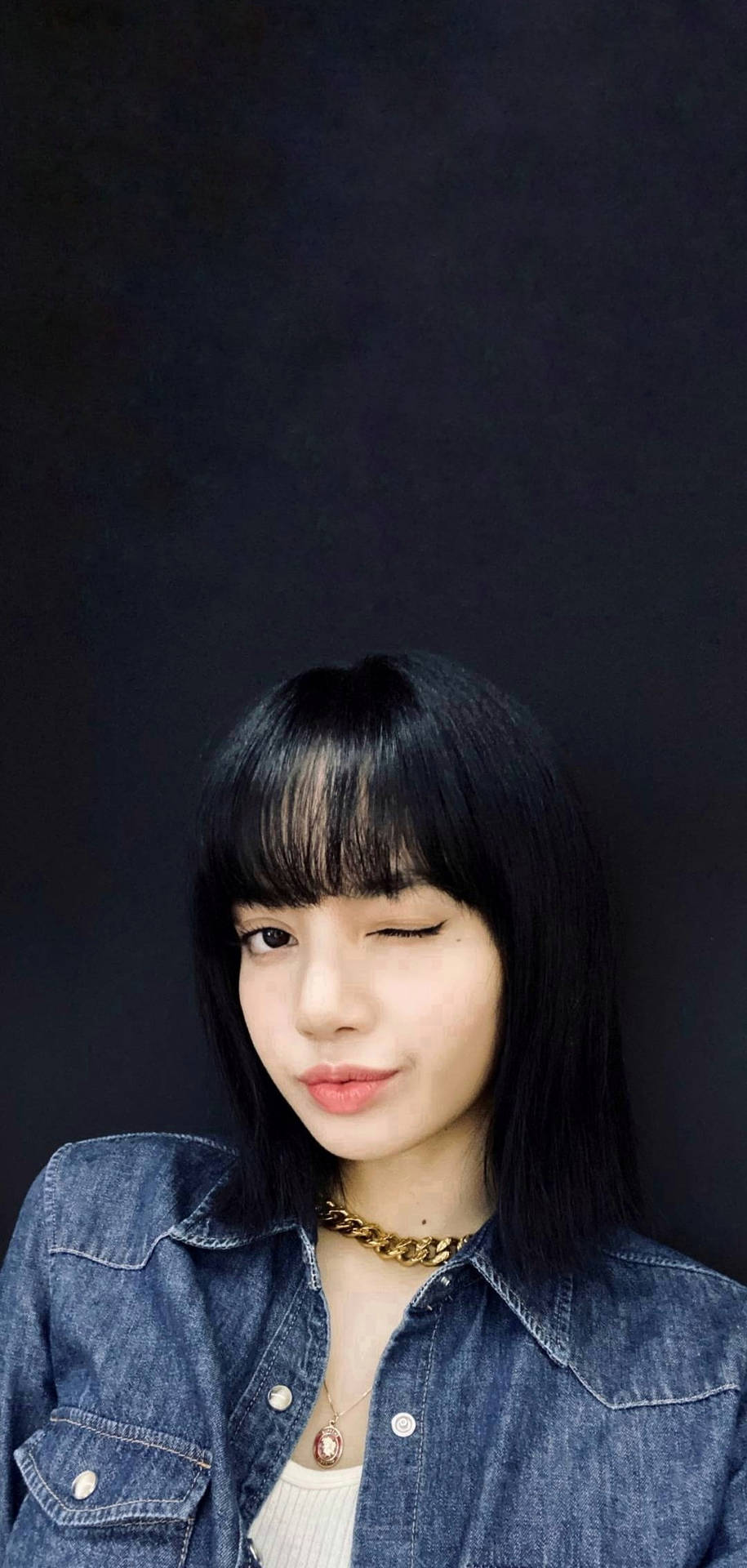 年輕女性身穿牛仔外套戴金鏈在深色背景前眨眼