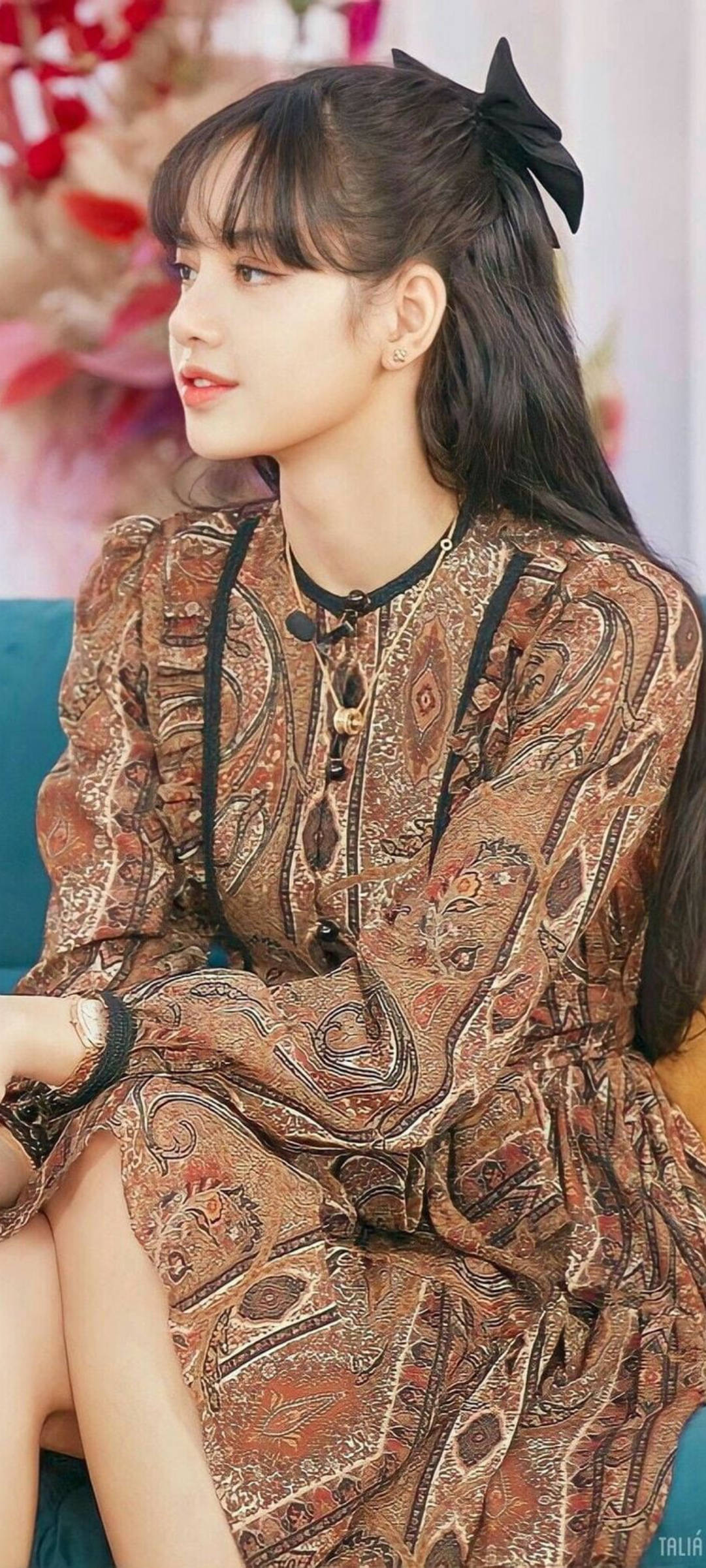 年輕女性身穿圖案連衣裙、戴黑色蝴蝶結坐在藍綠色沙發上