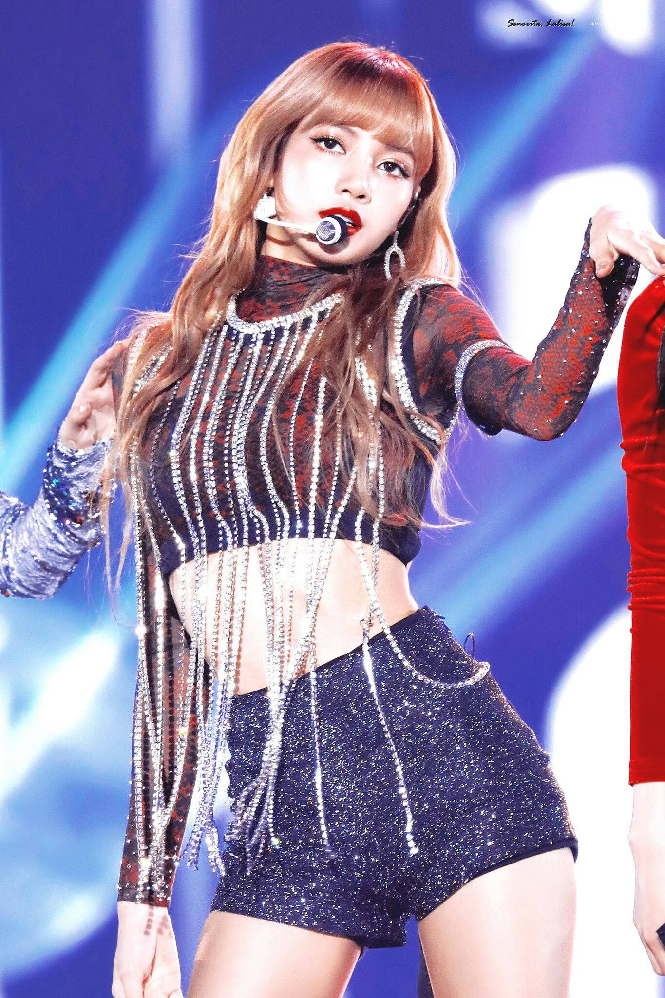 Lisa Manoban身著Sheesh紅色露臍上衣 壁紙 — 一位身穿閃亮銀黑色服裝的女表演者在明亮的藍色舞台燈光下對著麥克風唱歌。