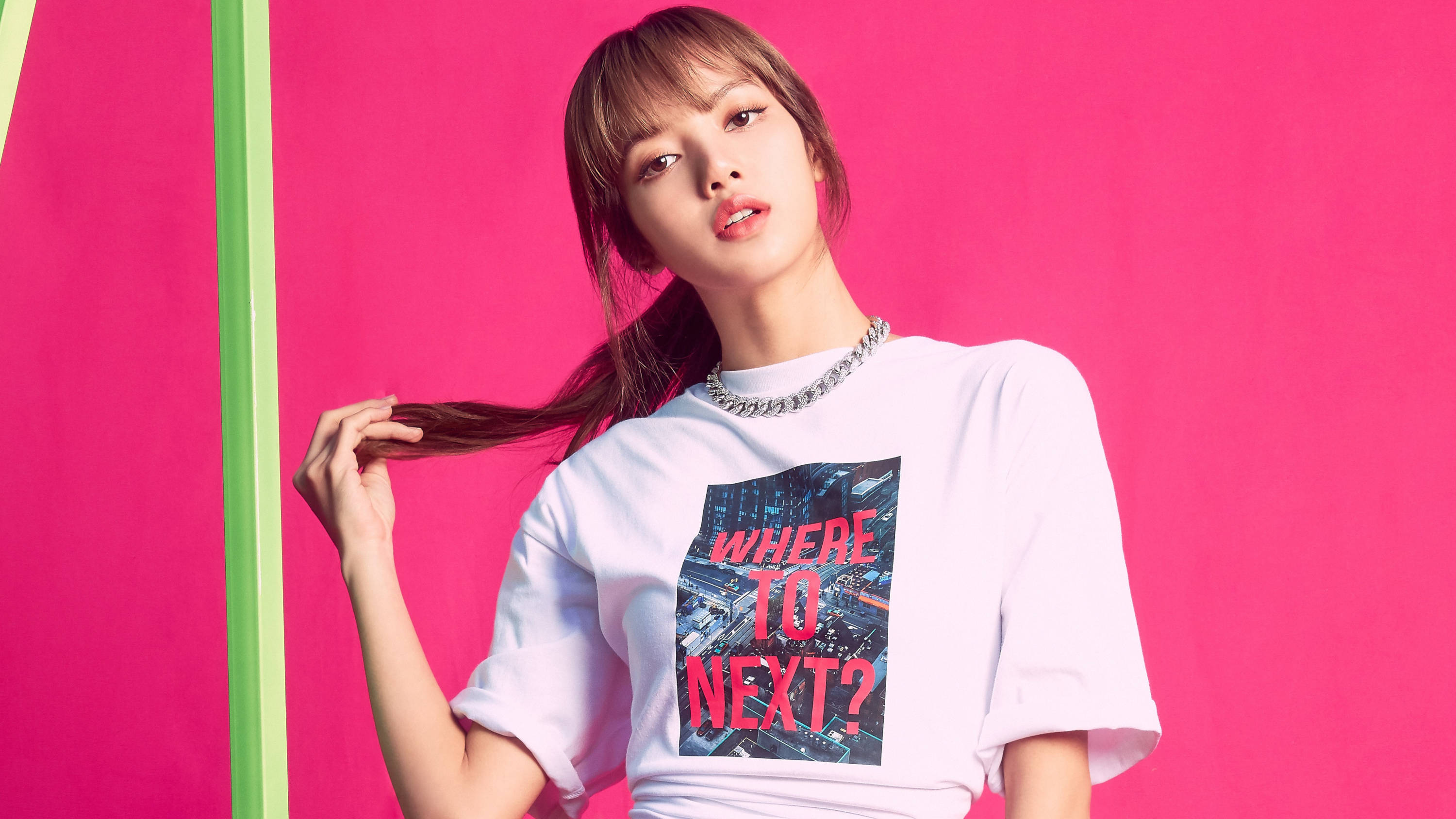 Lisa 輕觸髮絲 BLACKPINK 桌面壁紙 壁紙 — 一位身穿印有城市圖案白色T恤的年輕女性，在充滿活力的粉紅色和綠色背景前擺姿勢。