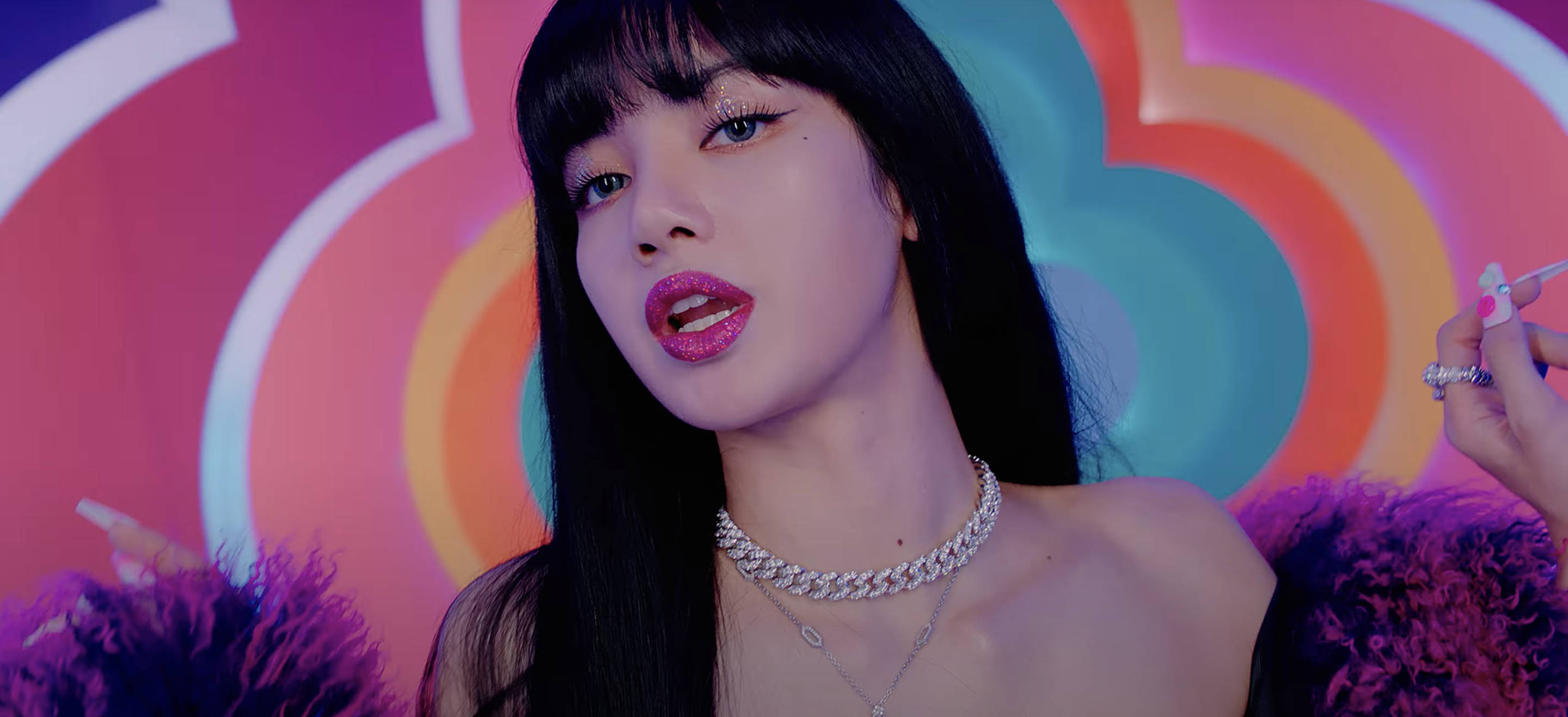 Lisa身著Sheesh毛絨外套拍攝《Ice Cream》MV 壁紙 — 一位黑髮粉紅唇膏的女性在充滿活力的彩虹漩渦背景前擺姿勢。