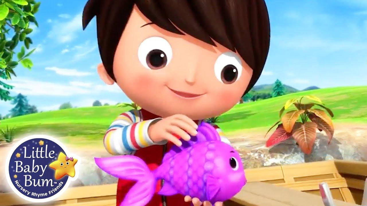 Little Baby Bum紫色小魚 壁紙 — 一個開心的卡通男孩在陽光明媚的戶外環境中拿著一個亮紫色的魚玩具，背景有綠色山丘和藍天。