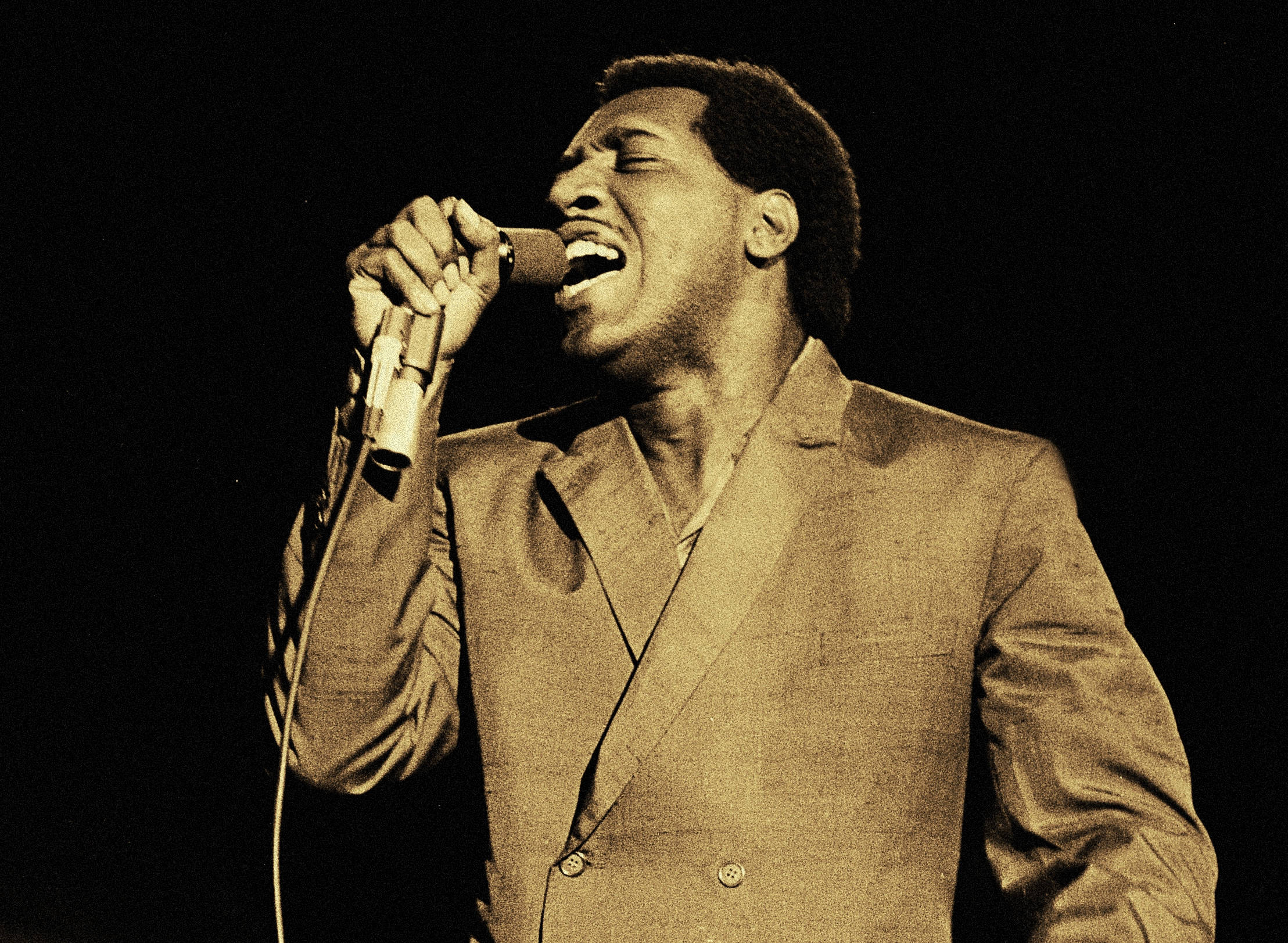 Little Walter 樂隊年代RnB演出照 壁紙 — 一張懷舊棕色調的照片捕捉到一位男歌手在黑暗舞台背景下，對著復古麥克風熱情演唱。