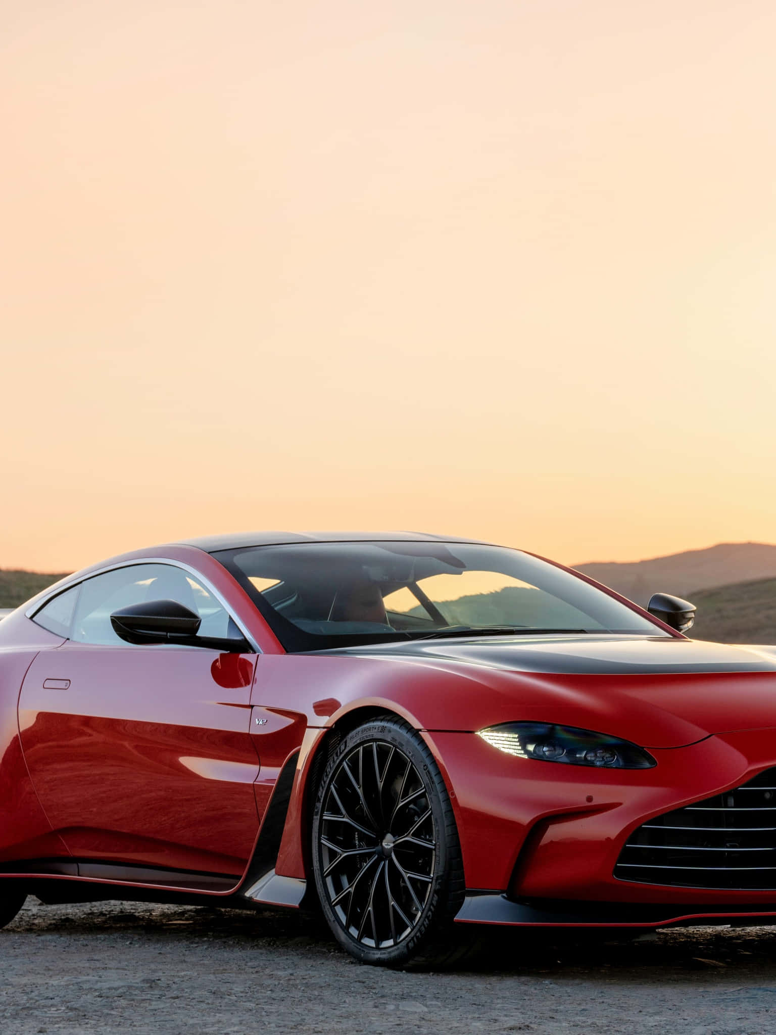 Aston Martin Vantage 桌布 壁紙 — 一輛流線型紅色跑車在溫暖的夕陽光下閃閃發光，背景是朦朧的沙漠地平線。