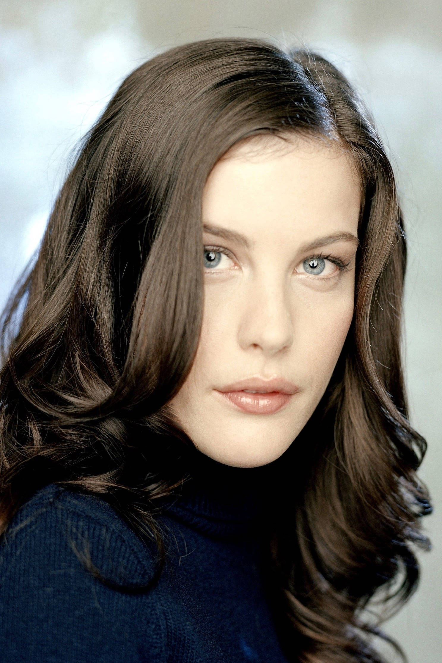 Liv Tyler 好萊塢明星肖像 壁紙 — 一位擁有長長棕色頭髮和引人注目的藍色眼睛的女性穿著深藍色高領毛衣的特寫肖像。