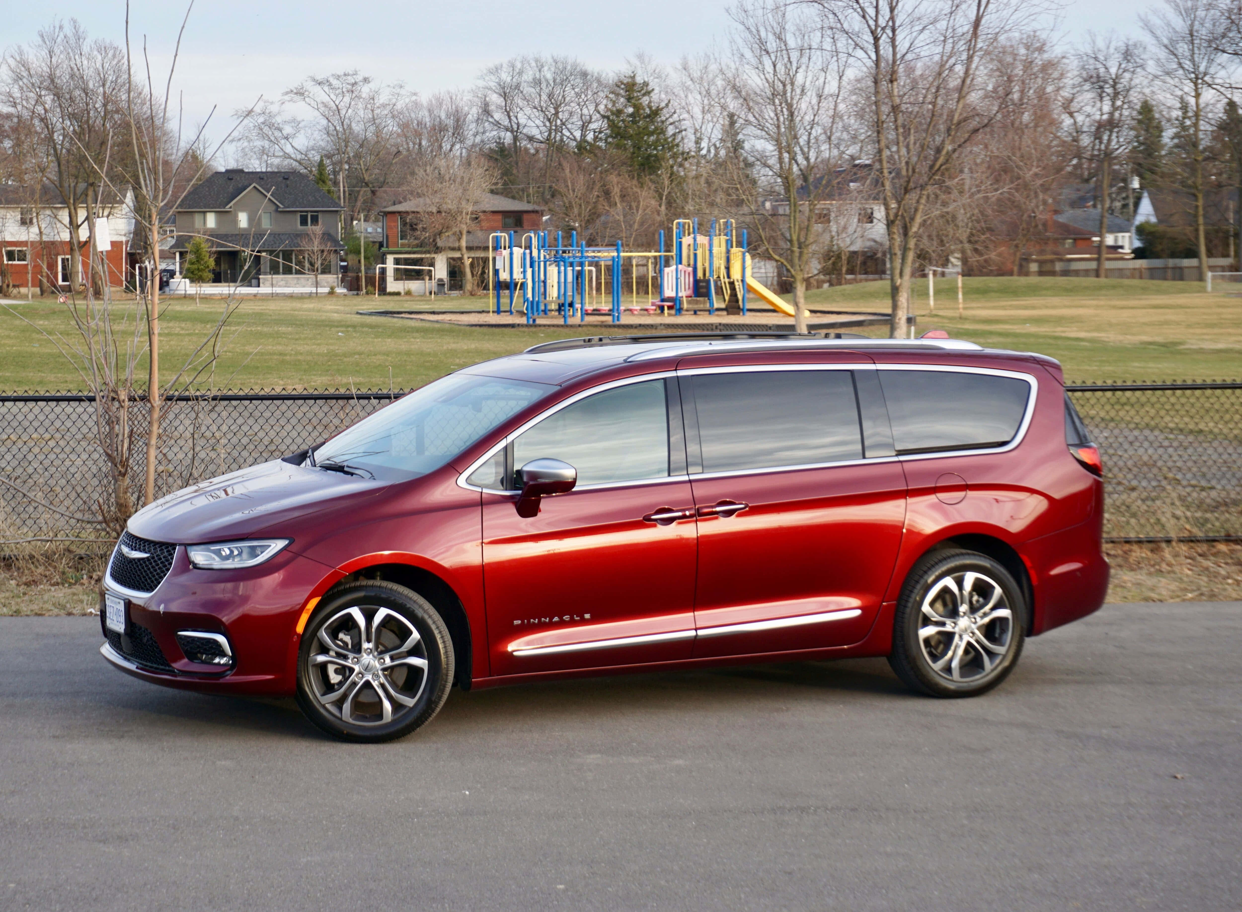 Chrysler Pacifica 桌布 壁紙 — 一架亮紅色嘅Chrysler Pacifica小型貨車泊喺瀝青路上，背景有遊樂場同光禿禿嘅樹。
