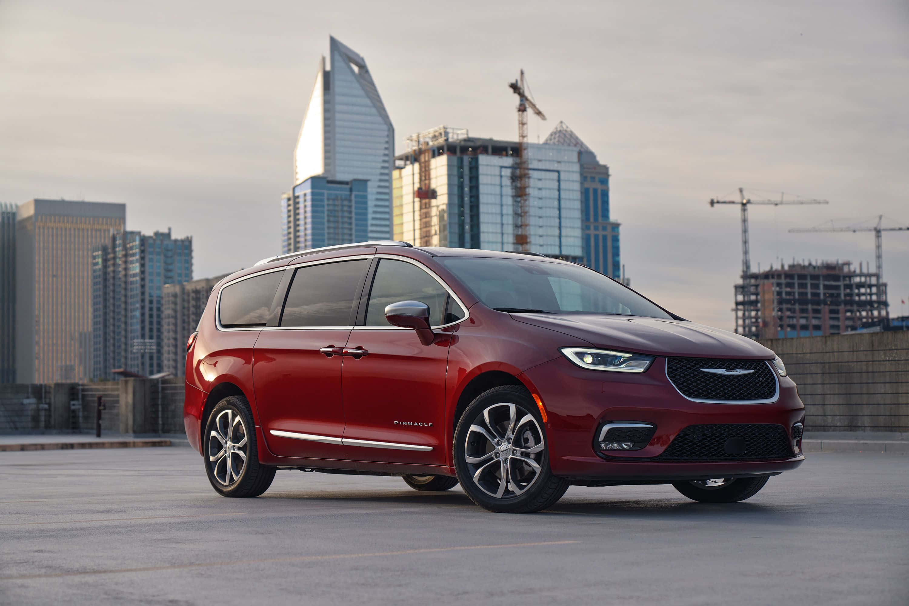 Chrysler Pacifica 桌布 壁紙 — 一架亮紅色嘅Chrysler Pacifica小型貨車停泊喺屋頂，背景係現代城市天際線同建築起重機。