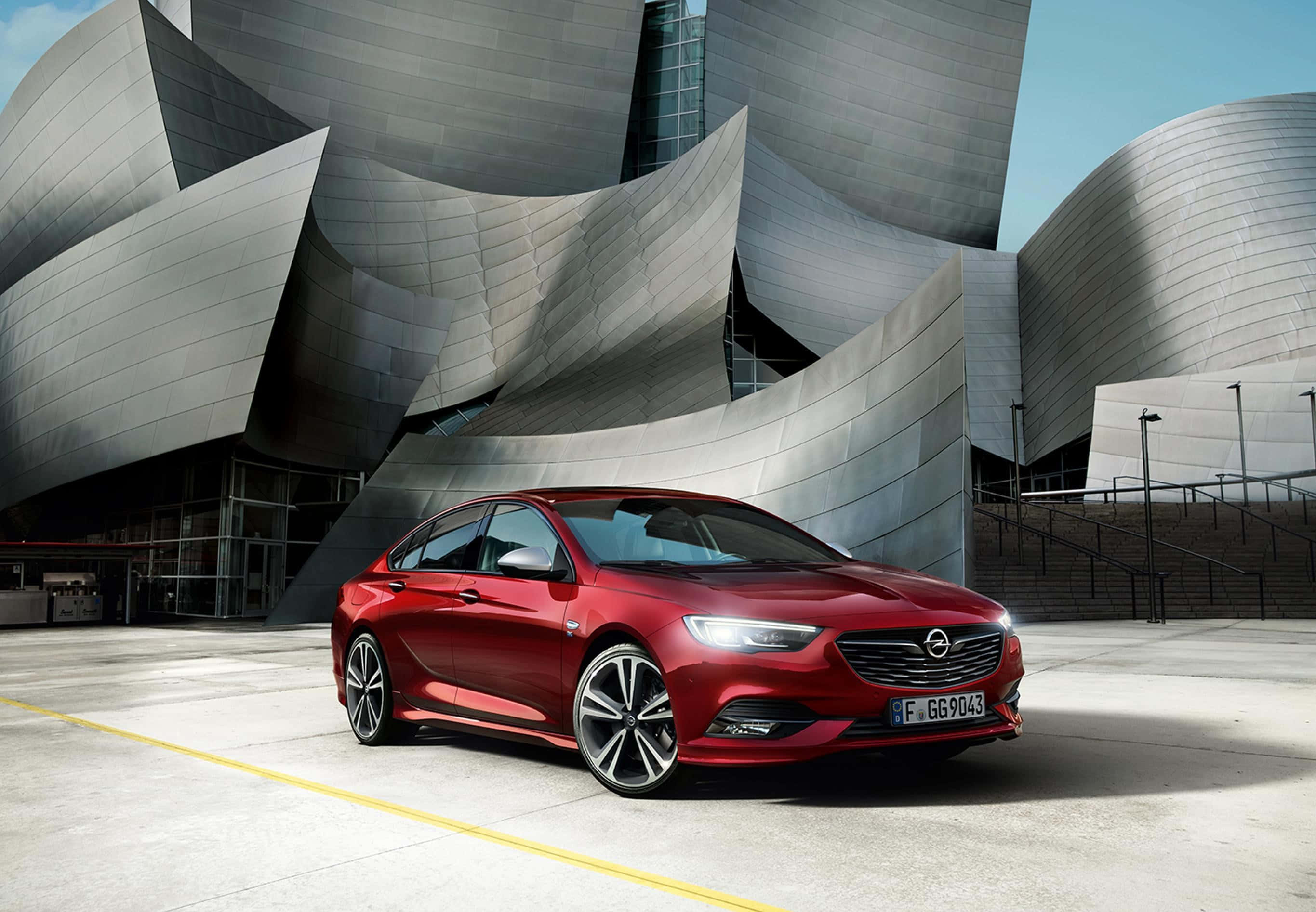 Opel Insignia 桌布 壁紙 — 一輛亮紅色嘅Opel房車停泊喺標誌性嘅鈦金屬外牆Walt Disney Concert Hall前面，喺明亮嘅日光下。