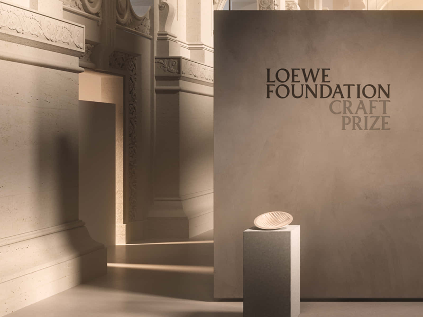 一個陶瓷碗放在陽光照射的畫廊基座上，牆上寫有「Loewe Foundation Craft Prize」文字。