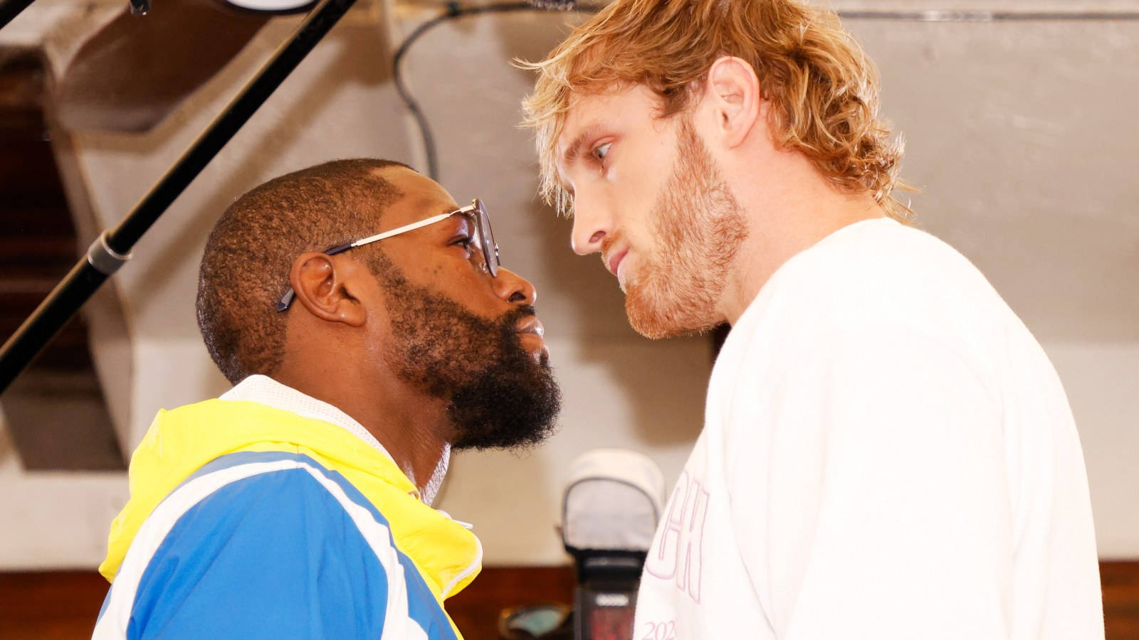 Logan Paul 與 Mayweather 激烈對決 壁紙 — 兩名男子在明亮的錄音室燈光下，附近有咪高峰，進行緊張的對峙。