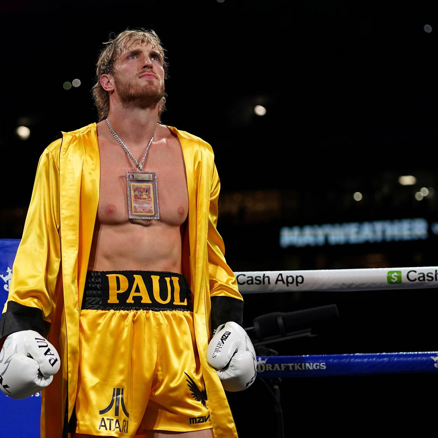 Logan Paul 擊戰前沉思 壁紙 — 一位肌肉發達的拳擊手穿著閃亮的黃色長袍和短褲，站在擂台上，帶著堅定的表情向上看。