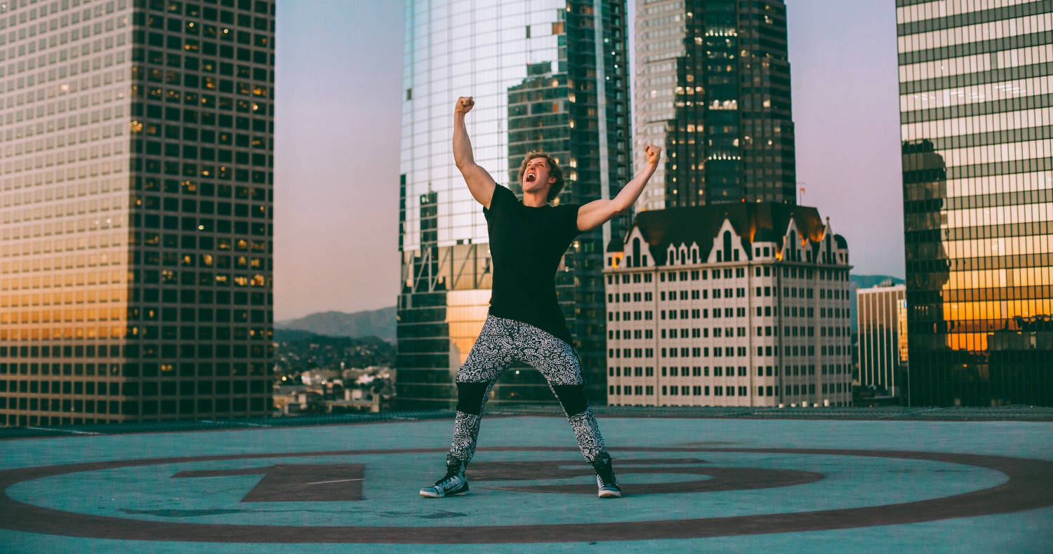 Logan Paul 快樂享受生活 壁紙 — 一個快樂的男人在屋頂直升機停機坪上高舉雙臂慶祝，金色的夕陽光芒灑在他身後的城市天際線上。