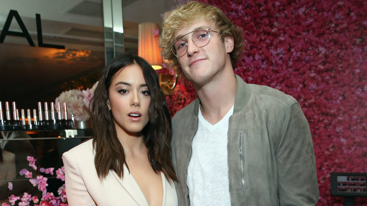 Logan Paul 與 Olivia 的甜蜜時光 壁紙 — 一名男子和一名女子在時尚的室內環境中，以充滿活力的粉紅色花卉牆為背景一起擺姿勢。