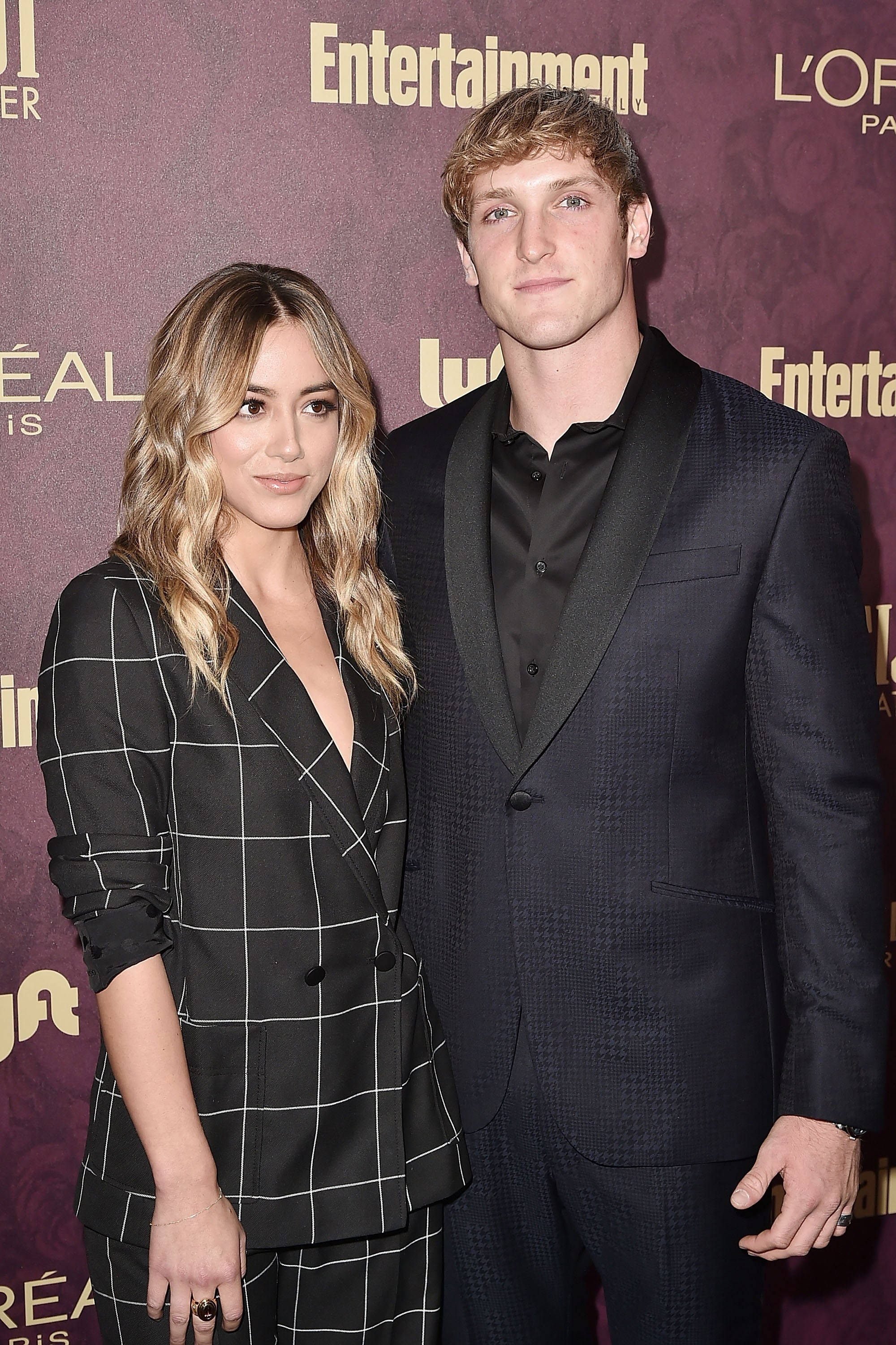 Logan Paul 與前女友 Chloe Bennet 壁紙 — 一名穿著正式服裝的男士和女士在帶有品牌背景的紅地毯活動上自信地擺姿勢。