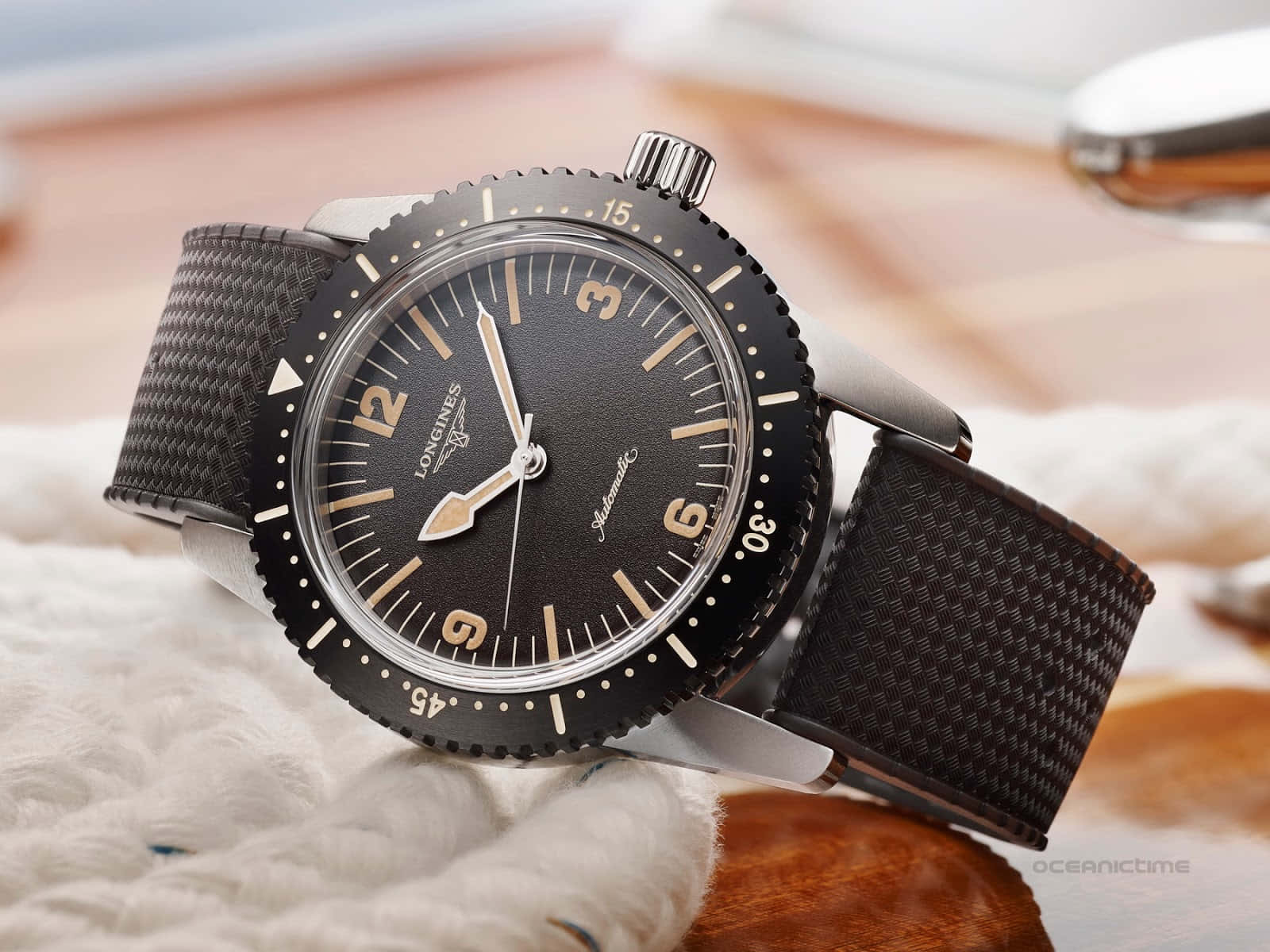 一隻黑色 Longines 手錶，帶有銀色點綴和紋理錶帶，放在白色布料表面上。