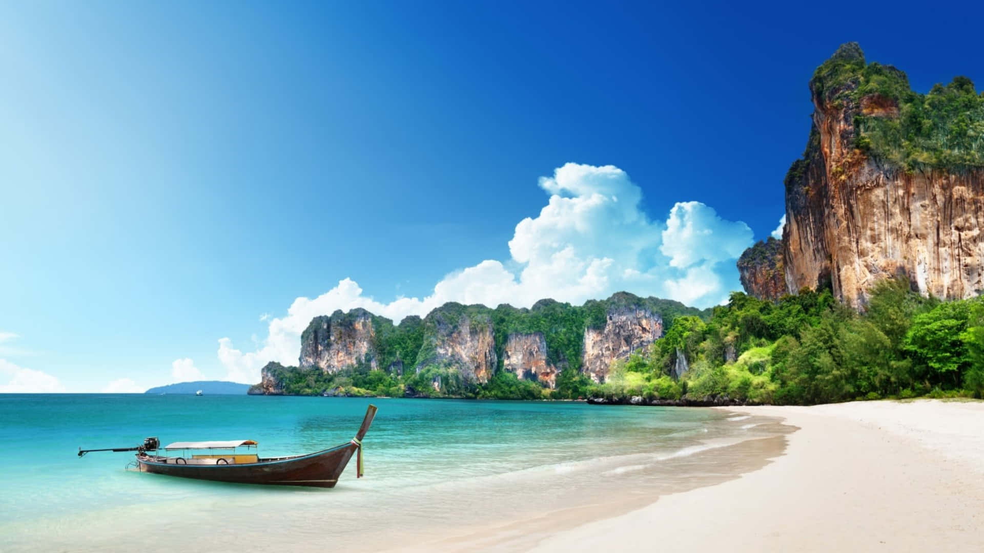 在寧靜4K海灘欣賞大自然之美 壁紙 — 一艘長尾船在碧綠海水旁的純白沙灘上休息，周圍是叢林覆蓋的懸崖，天空湛藍明亮。