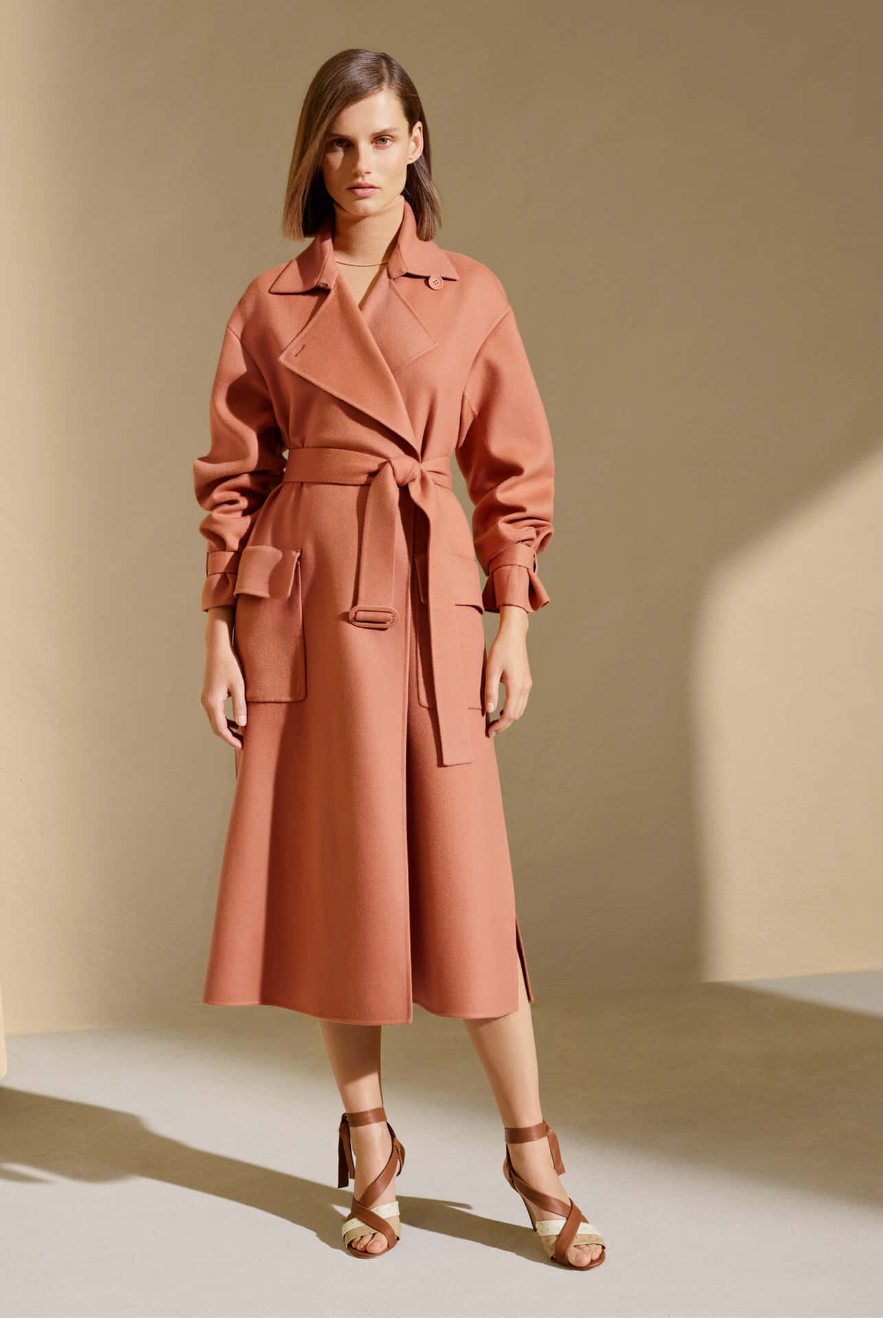 在簡約的工作室環境中，一位女性穿著鏽色風衣和繫帶涼鞋。