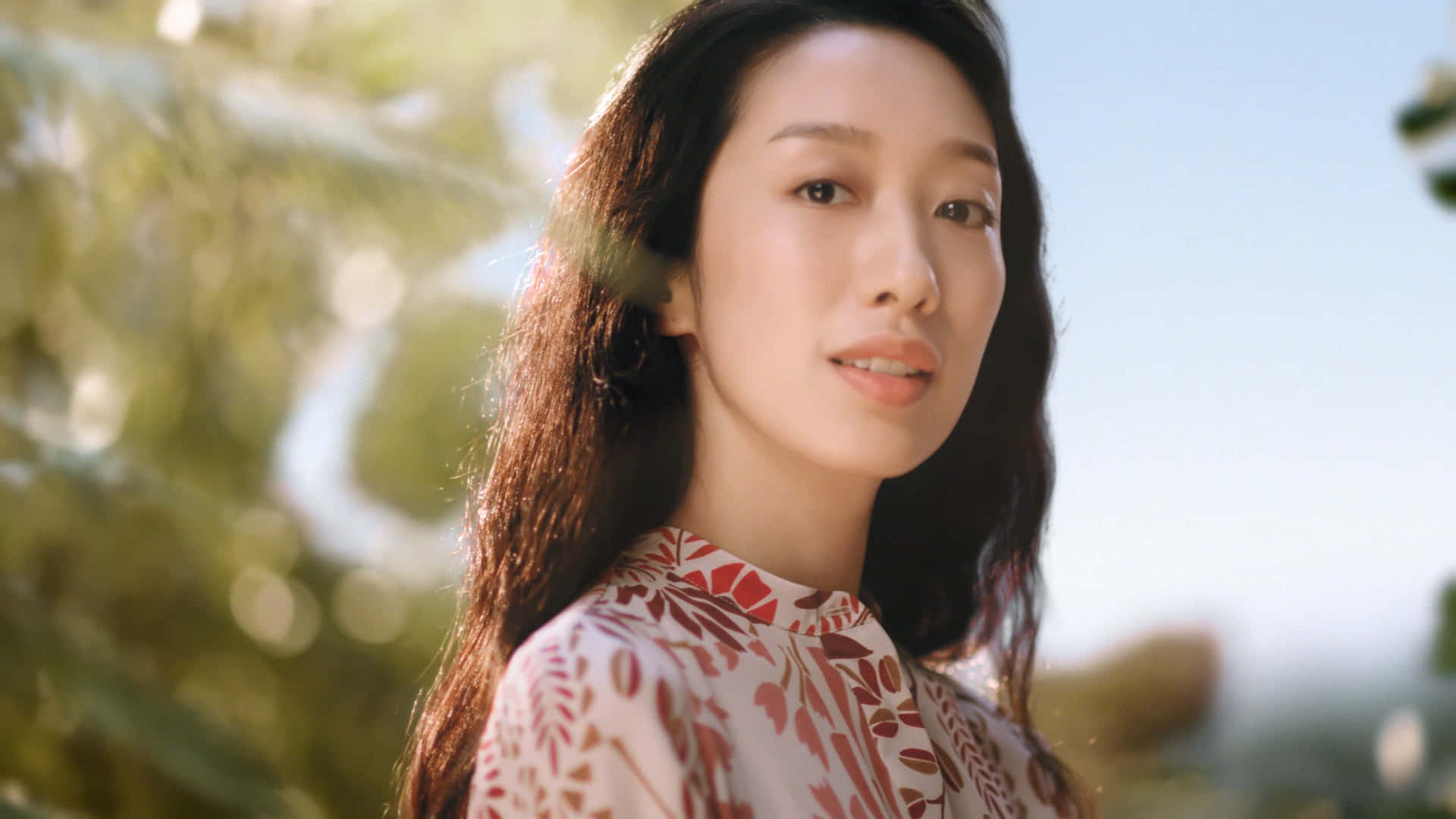 一位穿著花卉圖案上衣的女性在戶外陽光下輕柔微笑。