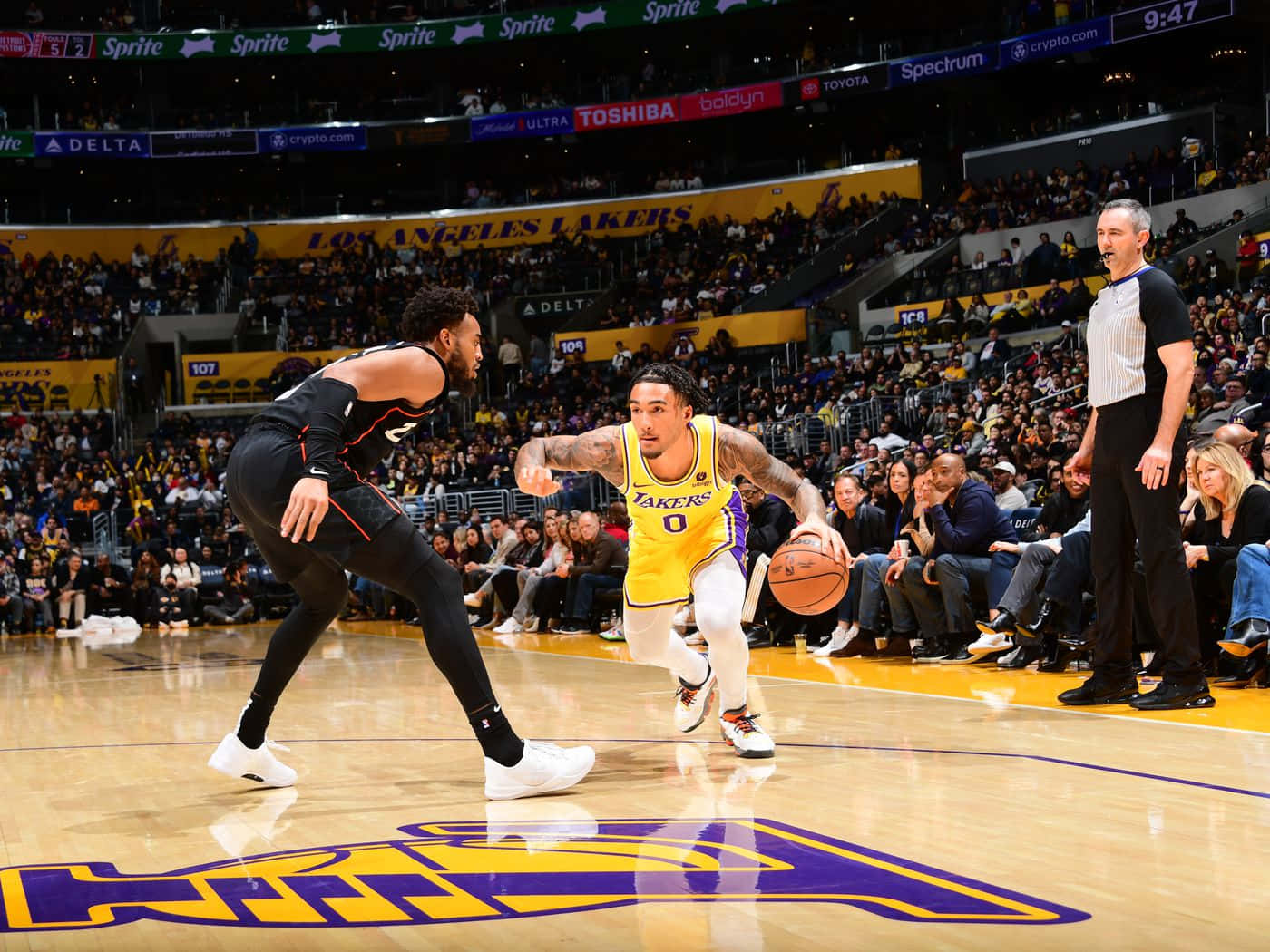  壁紙 — 一位身穿黃色球衣的洛杉磯湖人球員在擠滿觀眾的NBA比賽中運球，同時被一位身穿黑色球衣的對手防守。