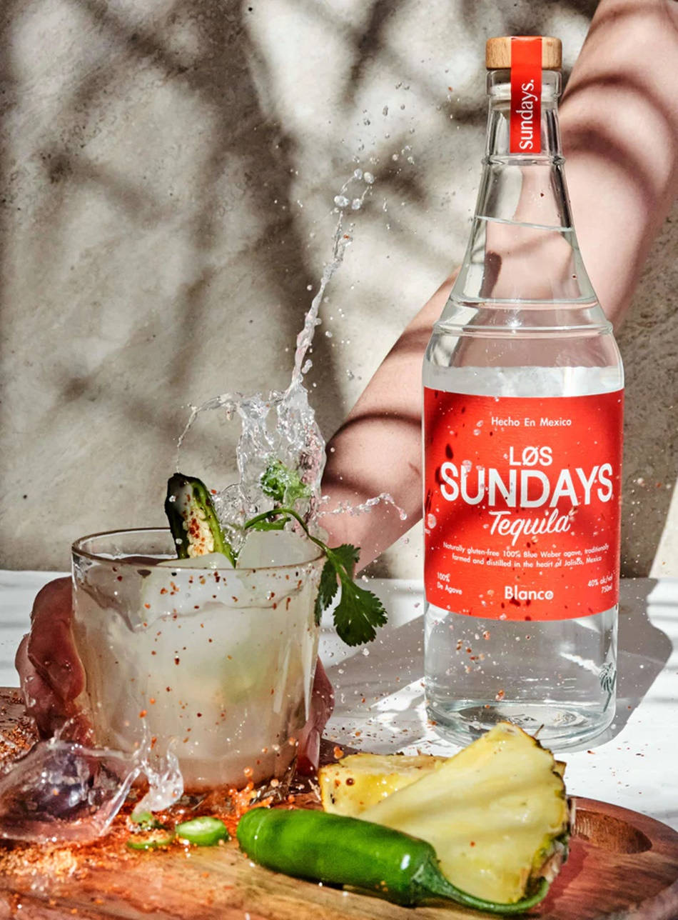 Los Sundays Blanco龍舌蘭酒 壁紙 — 一隻手將龍舌蘭酒倒入玻璃杯中，濺起水花，同時菠蘿、墨西哥辣椒和芫荽裝飾飲品。