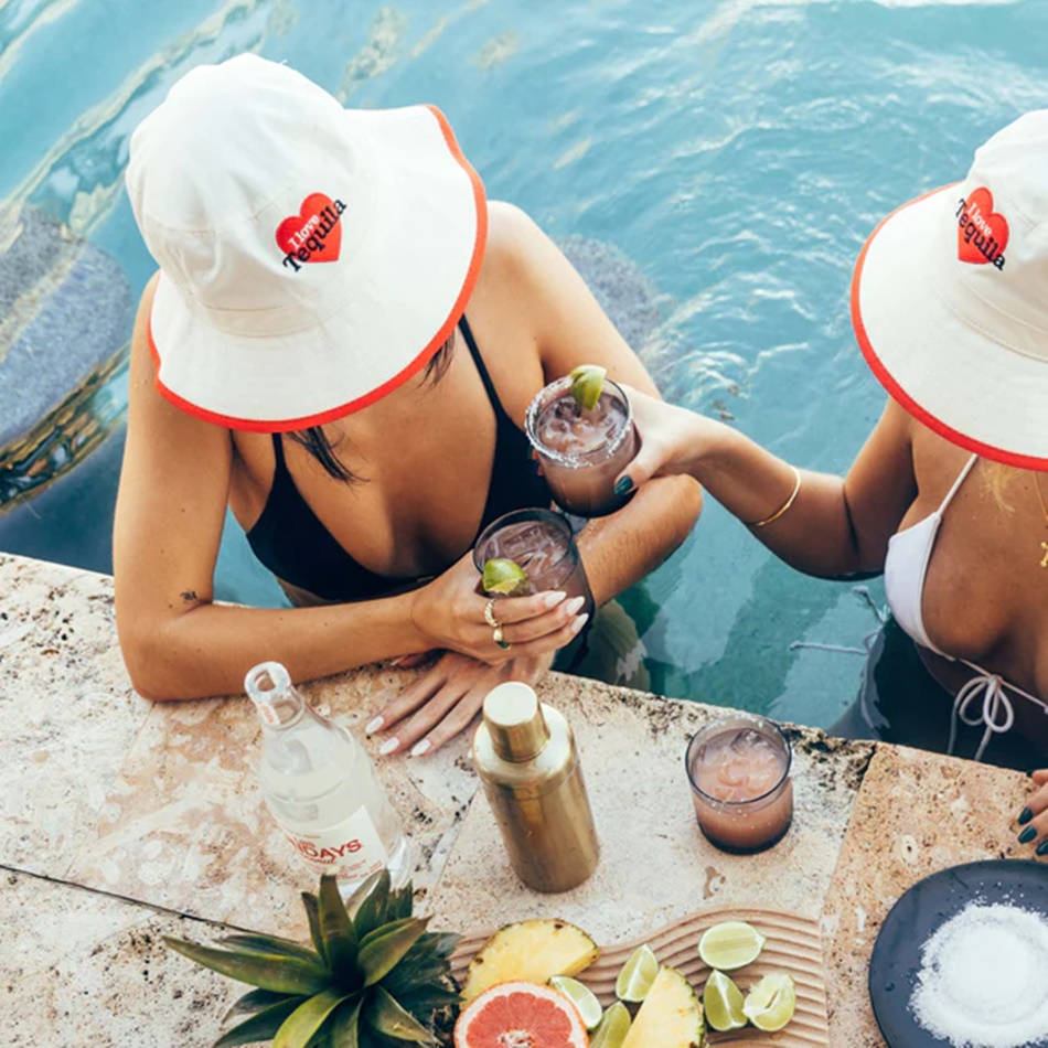 Los Sundays 青檸與漁夫帽 壁紙 — 兩位戴著白色「I heart tequila」漁夫帽的女性，在泳池邊的酒吧，周圍環繞著熱帶水果和鹽，用瑪格麗特雞尾酒乾杯。