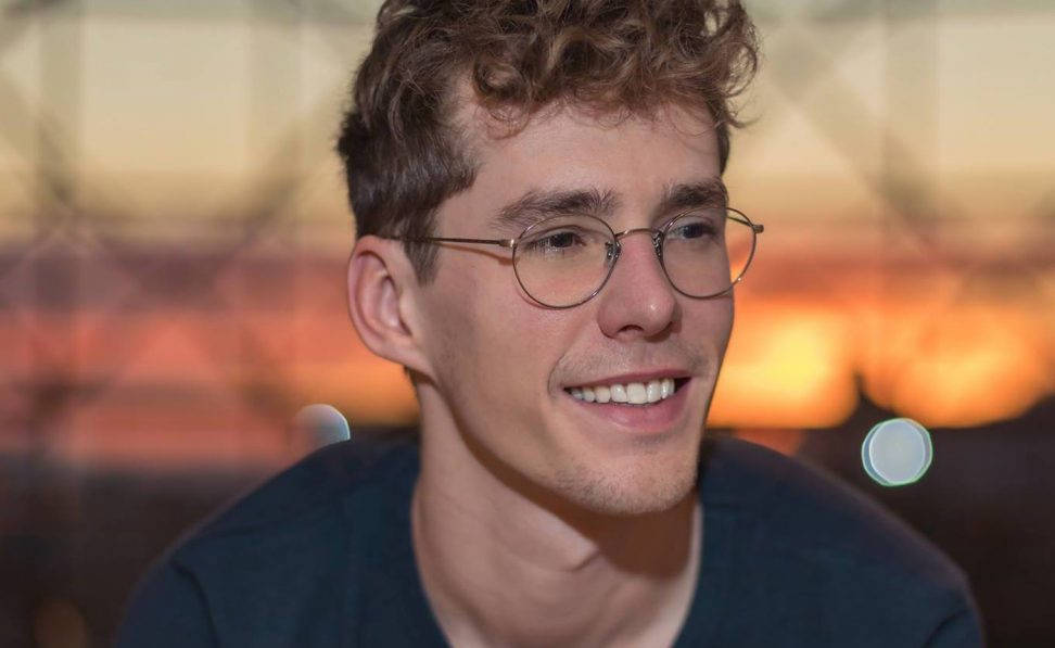 戴眼鏡的年輕男子在柔和光線的室內環境中溫暖地微笑。
